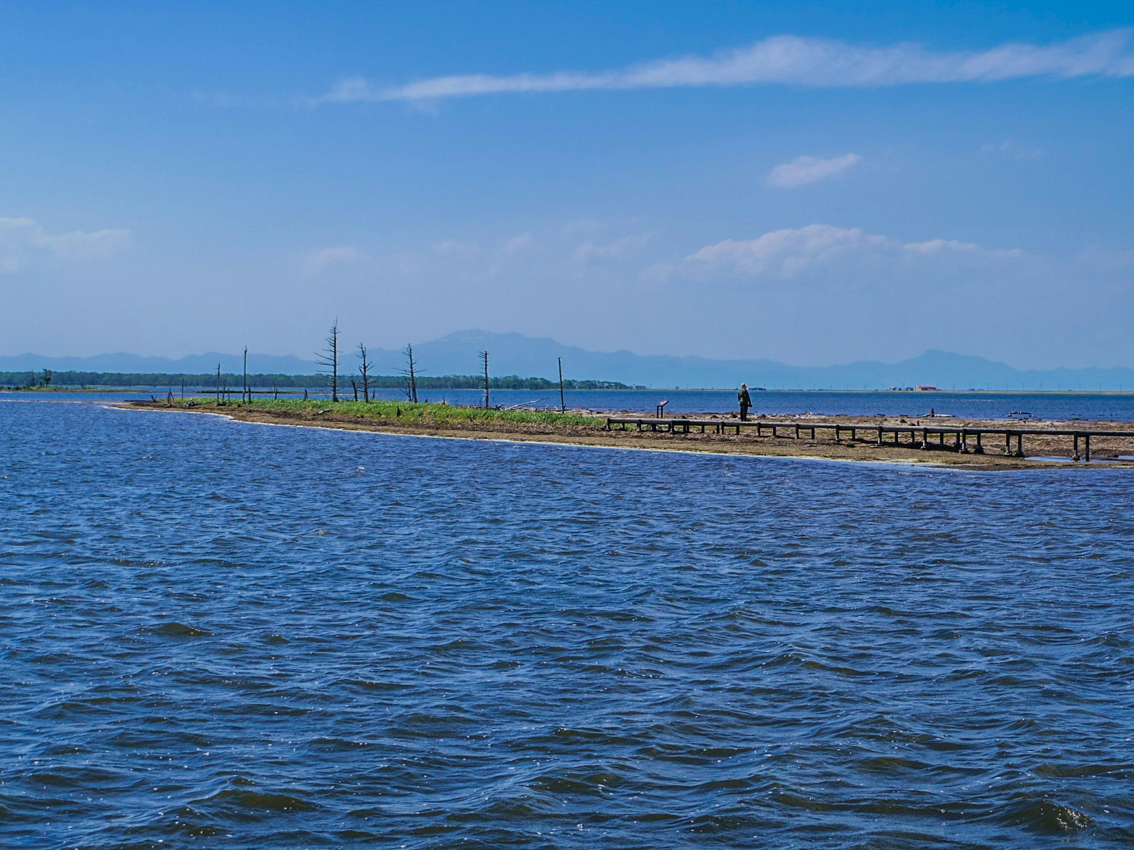 A narrow sandbar stretches across the blue water under a clear sky