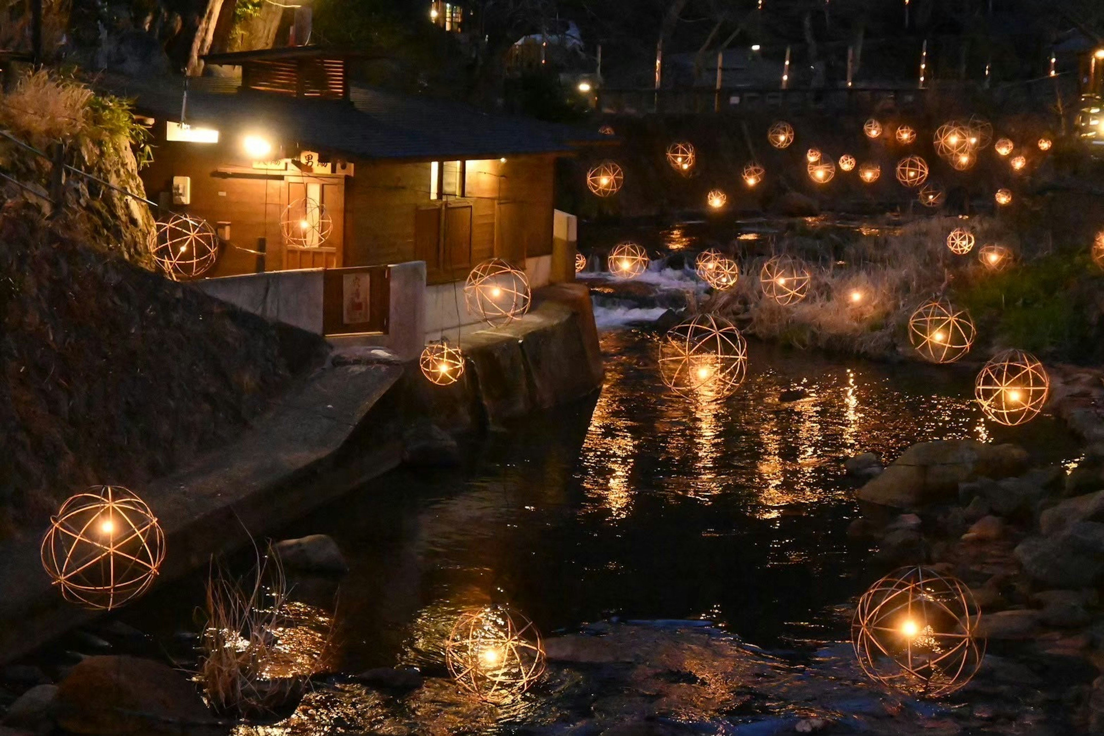 Scenic view of lanterns floating on a river by a wooden cabin at night