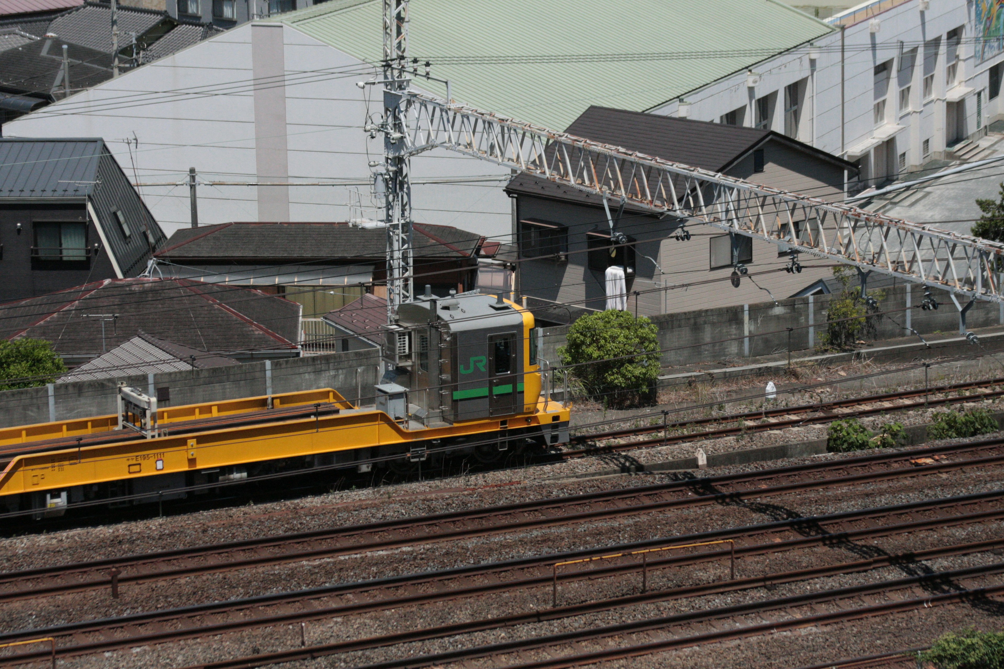 Yellow maintenance vehicle running alongside railway tracks in an urban setting