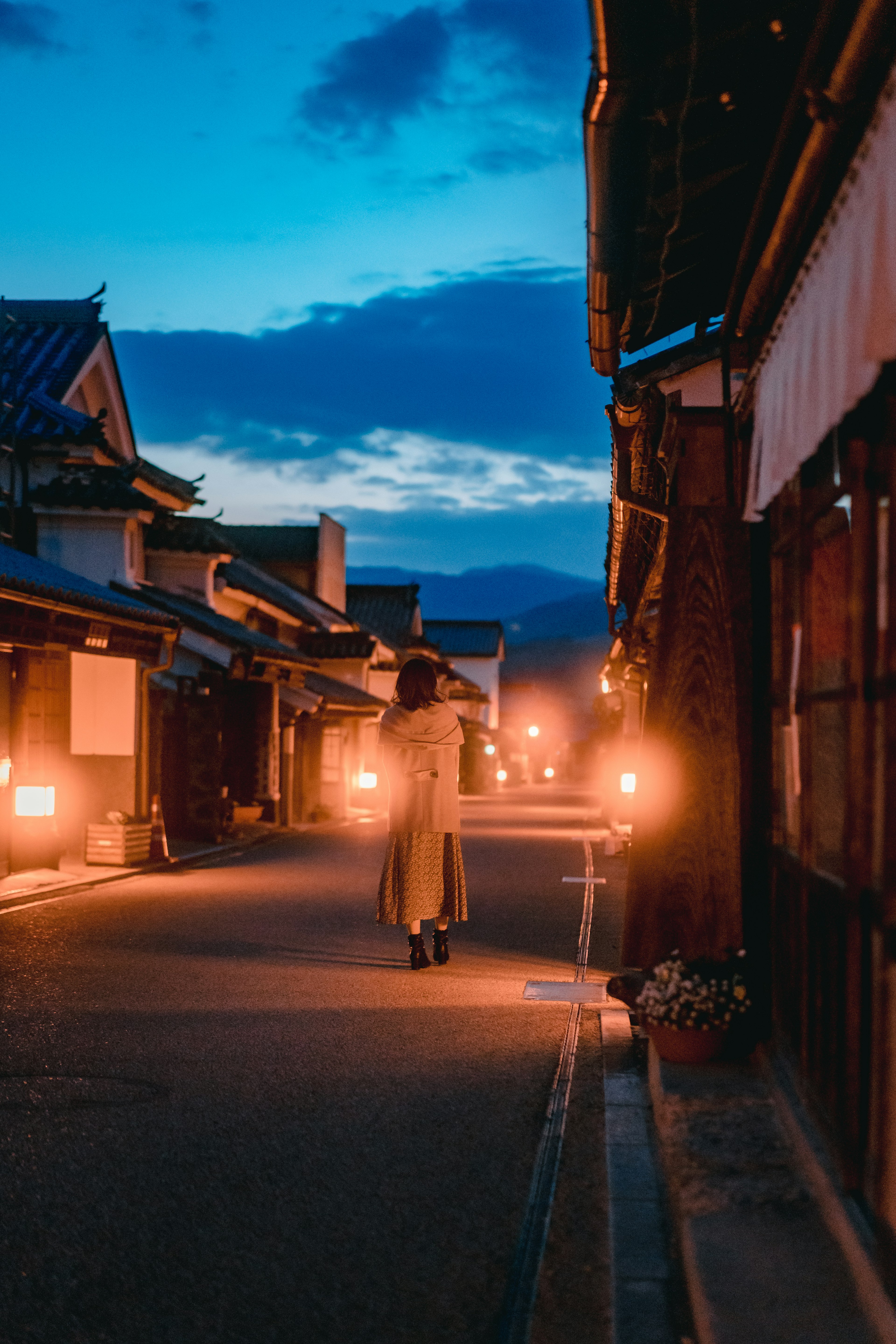 Woman walking in a quiet street at dusk with lanterns illuminating the path