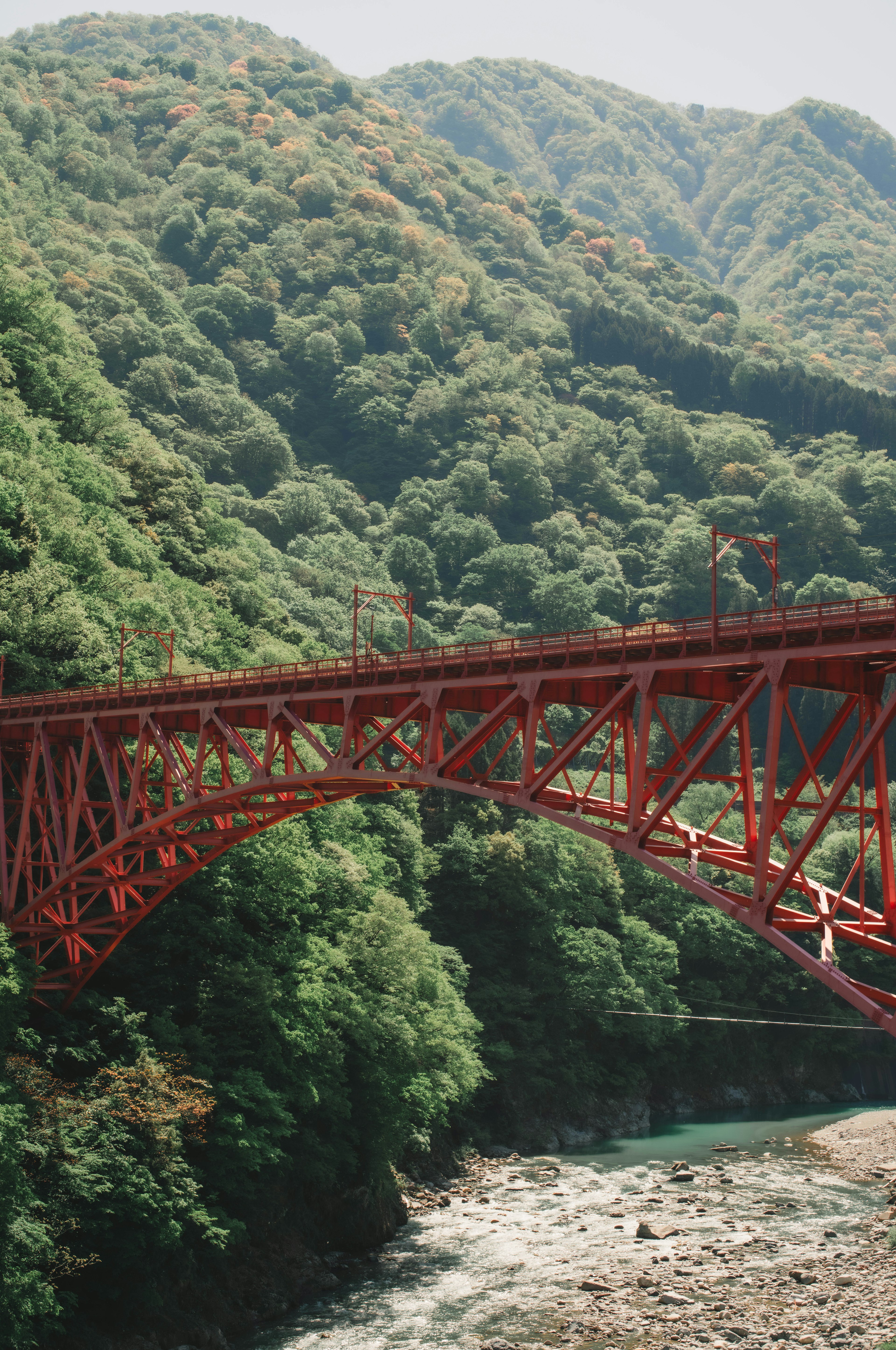 紅色鐵橋橫跨河流，背景是郁郁蔥蔥的綠色山脈