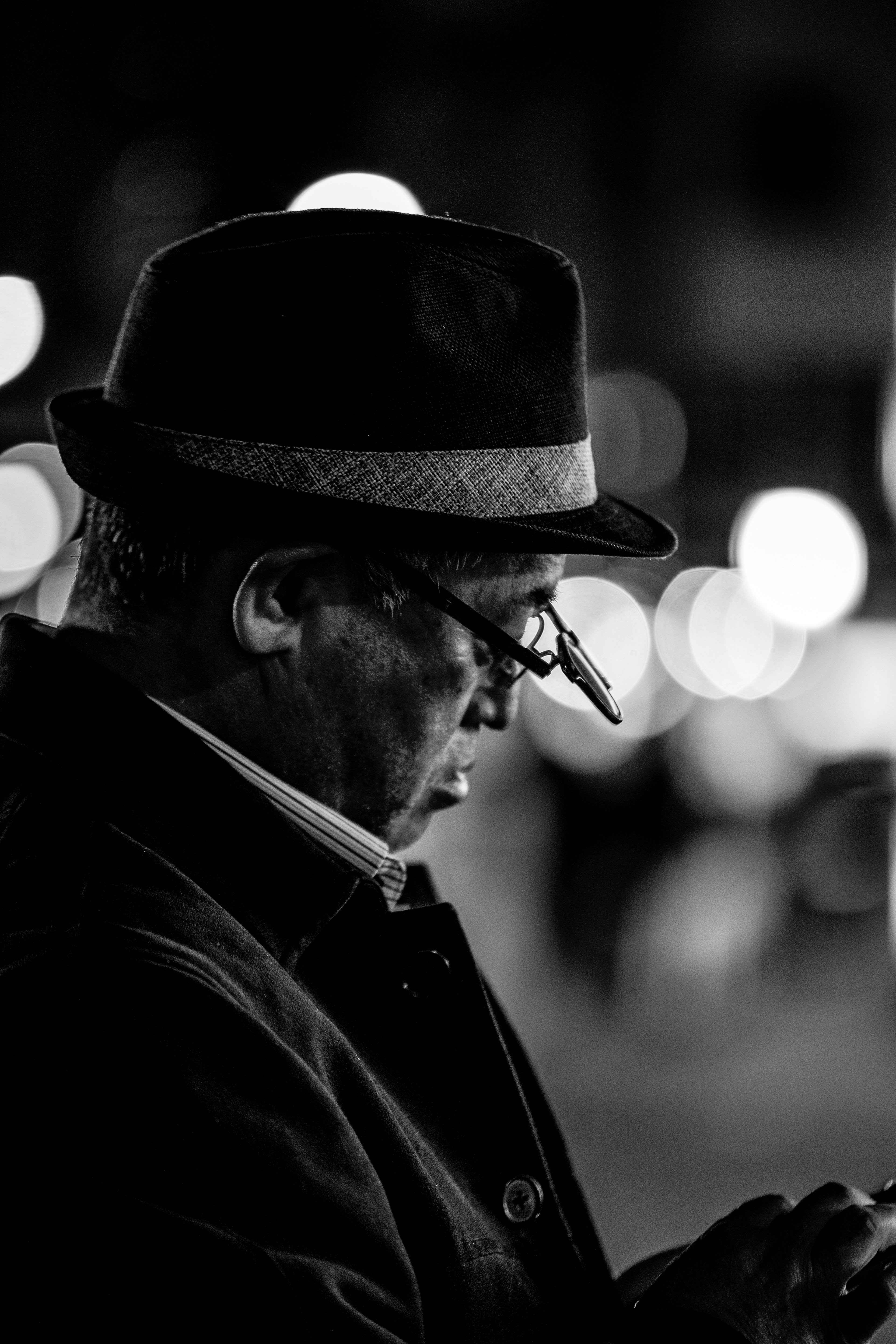 A man in a black hat looking at a smartphone in a monochrome image