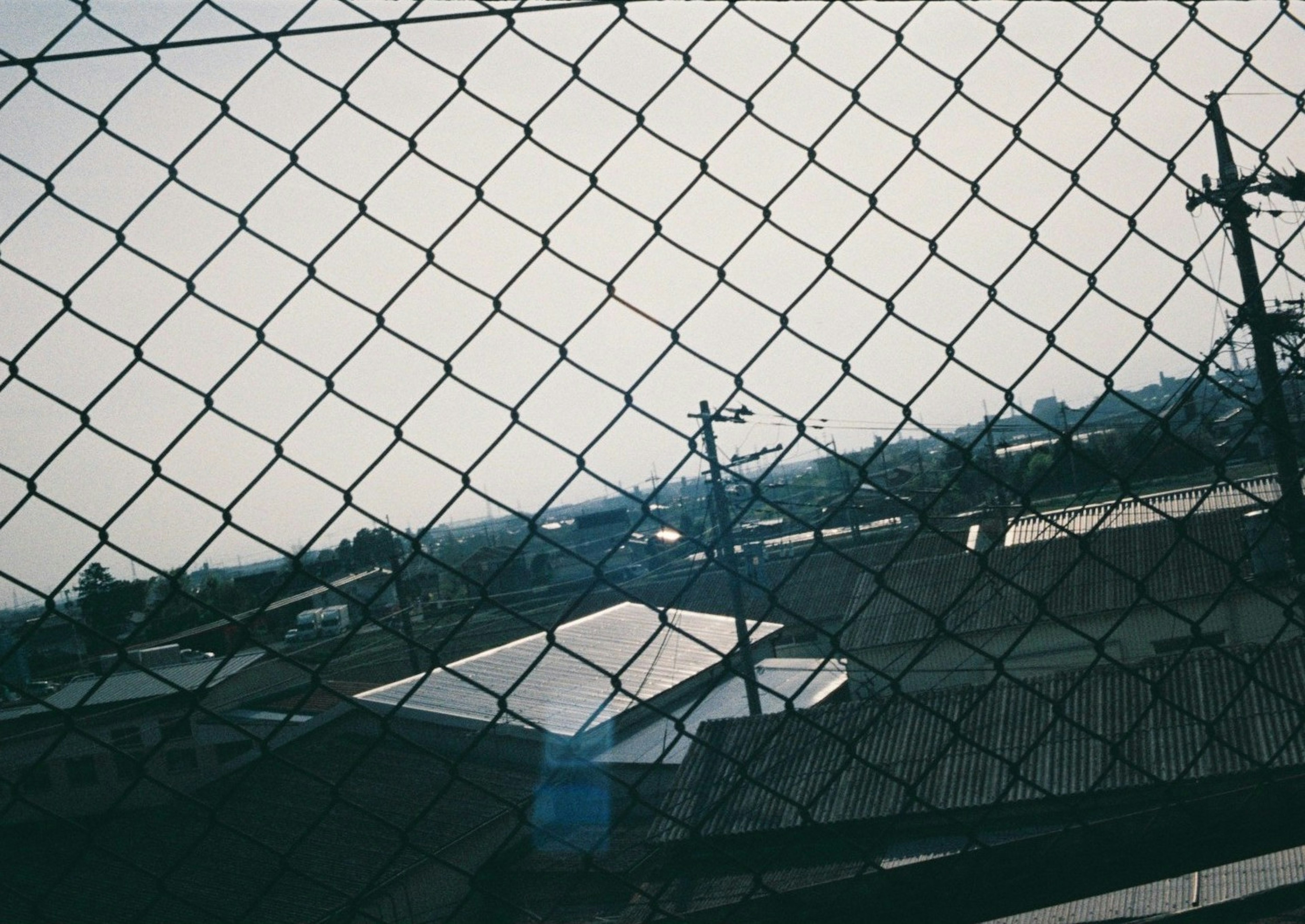 Cityscape viewed through a chain-link fence with utility poles