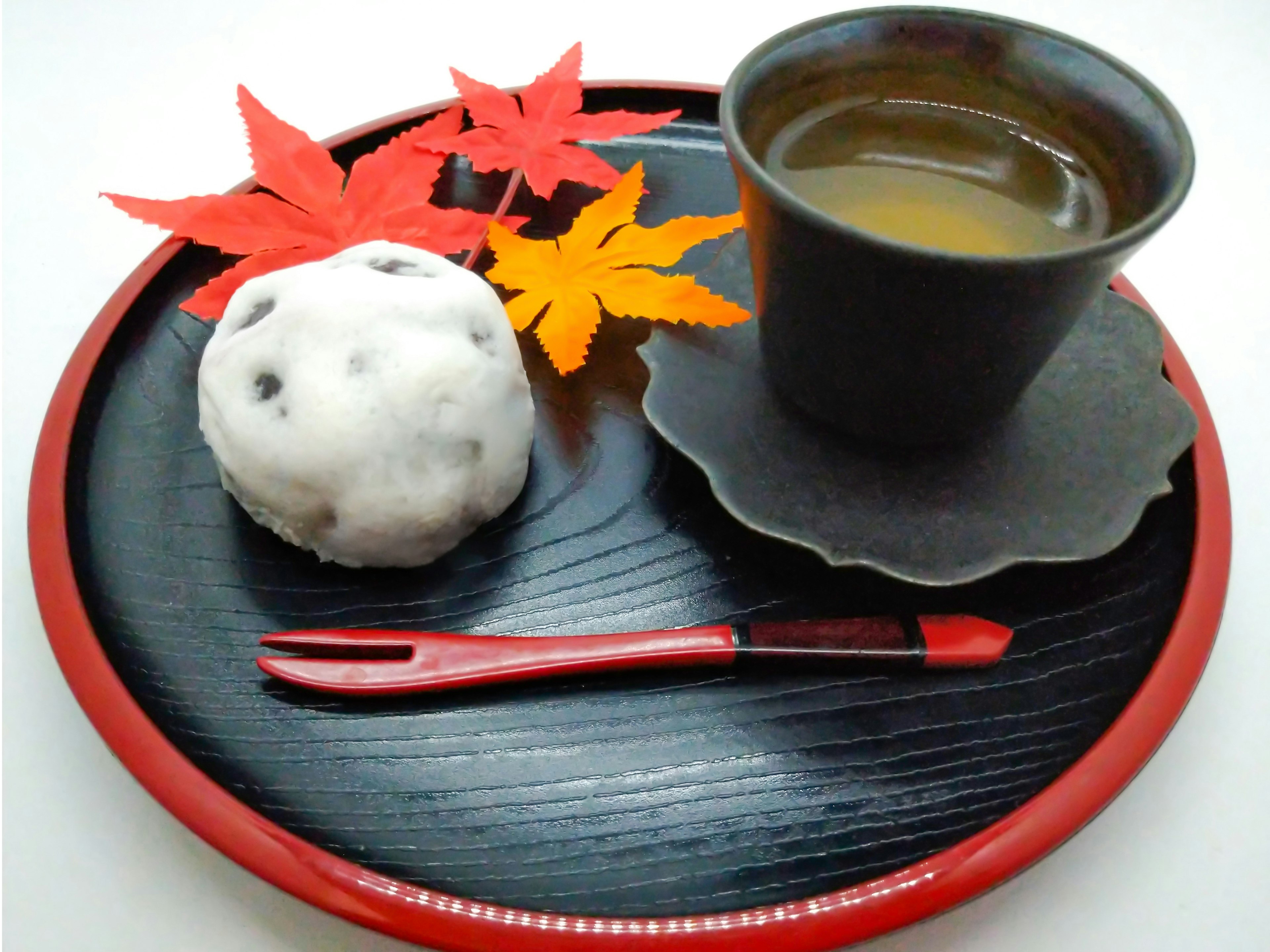 Un plato bellamente dispuesto con hojas de otoño y dulces japoneses acompañado de una taza de té