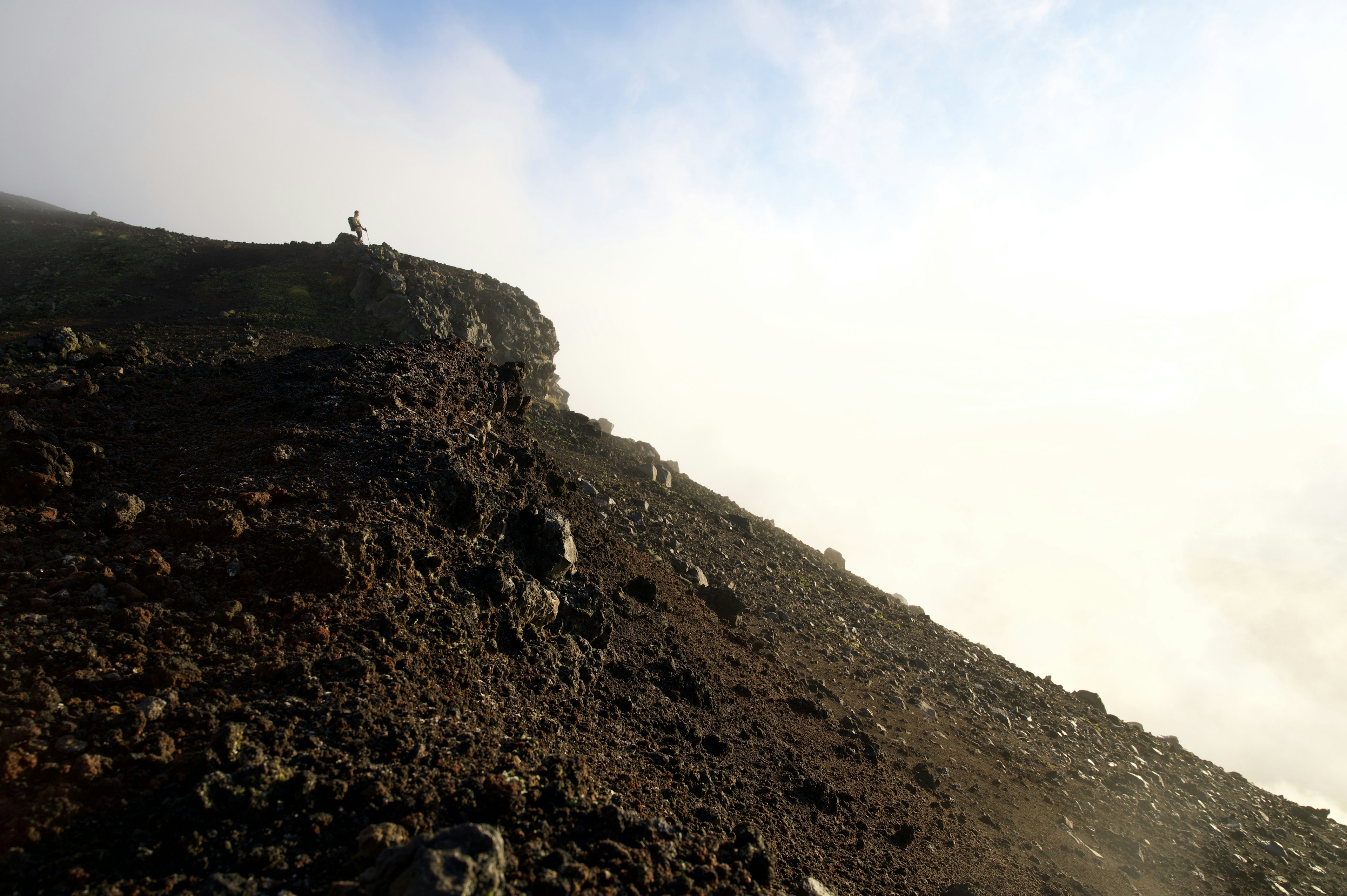 一个人站在火山坡上，背景有雾和云