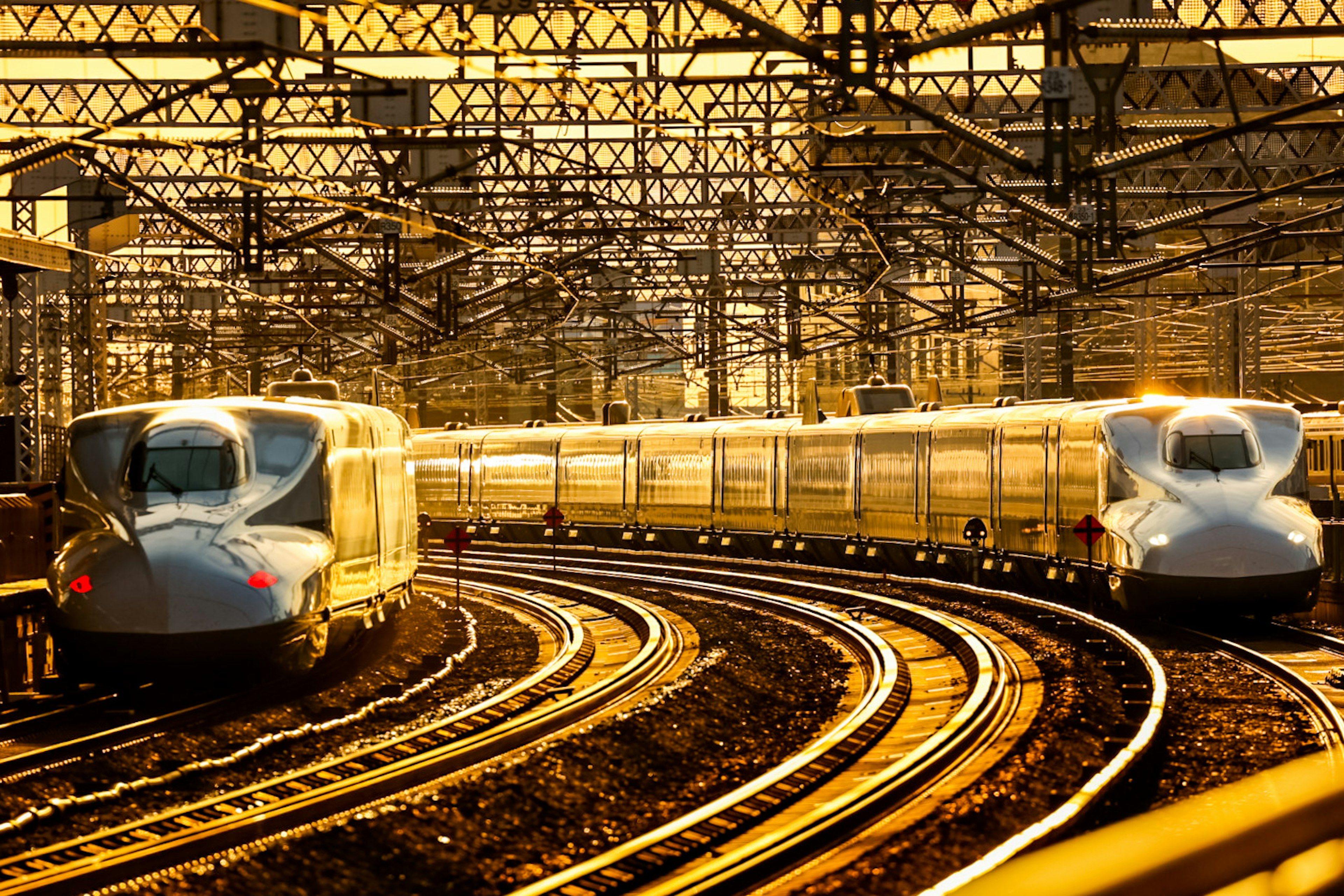 Two Shinkansen trains curving on tracks at sunset in a railway station