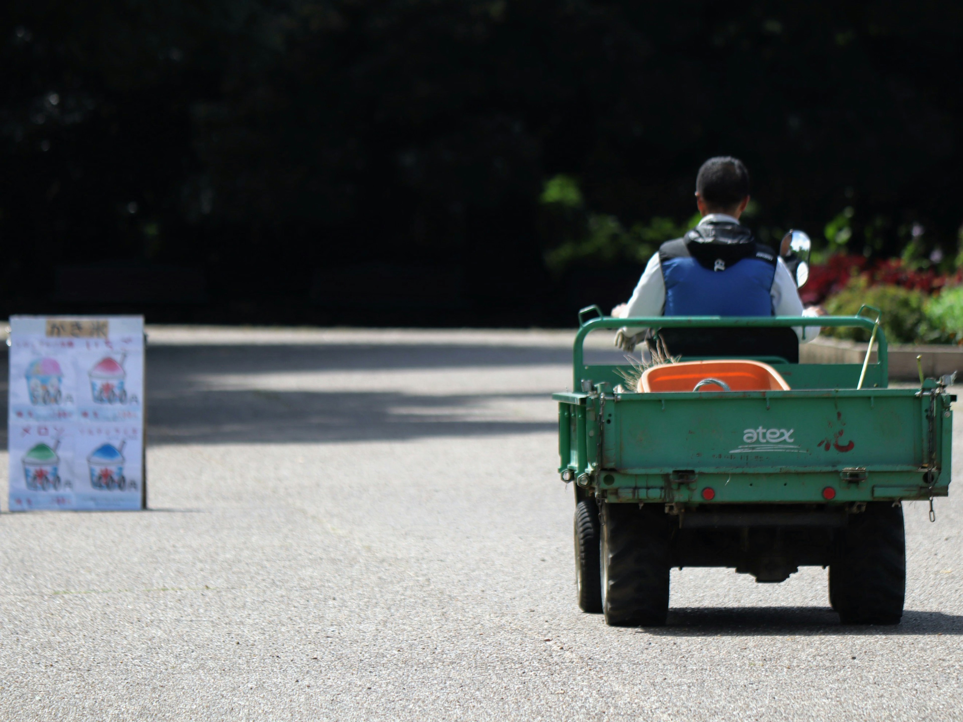 Person driving a small green vehicle on a road with signs in the background