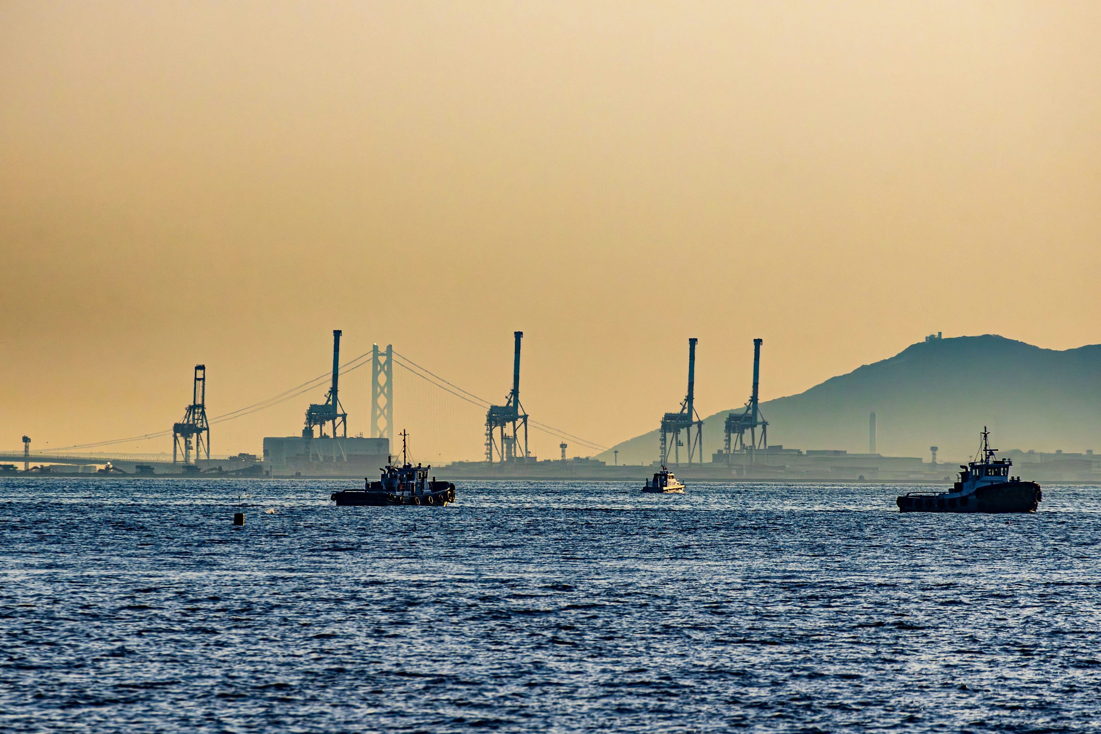 Silhouette di barche e strutture industriali al tramonto sull'oceano