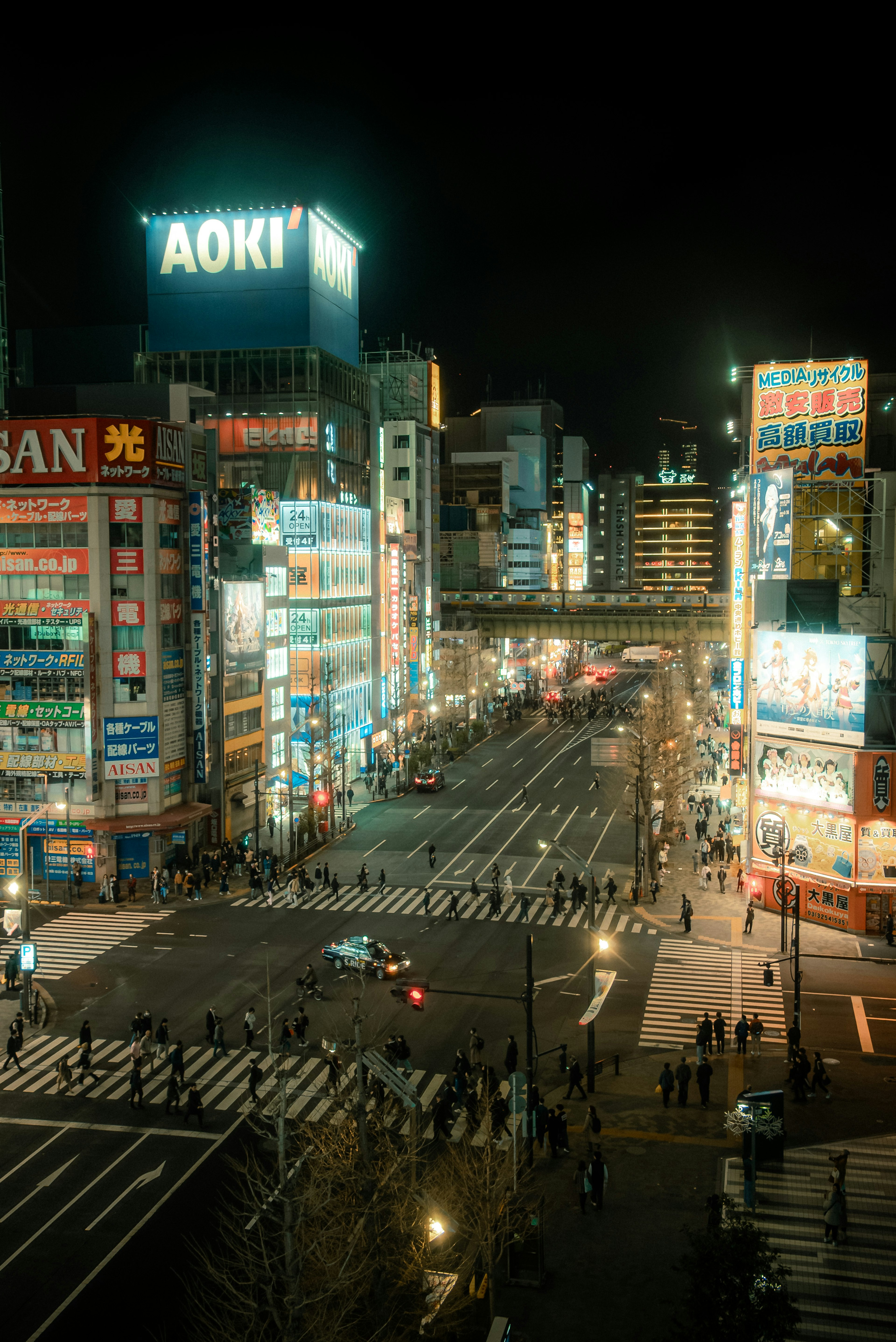 夜の都市風景で、AOKIの看板が目立つ交差点の全景