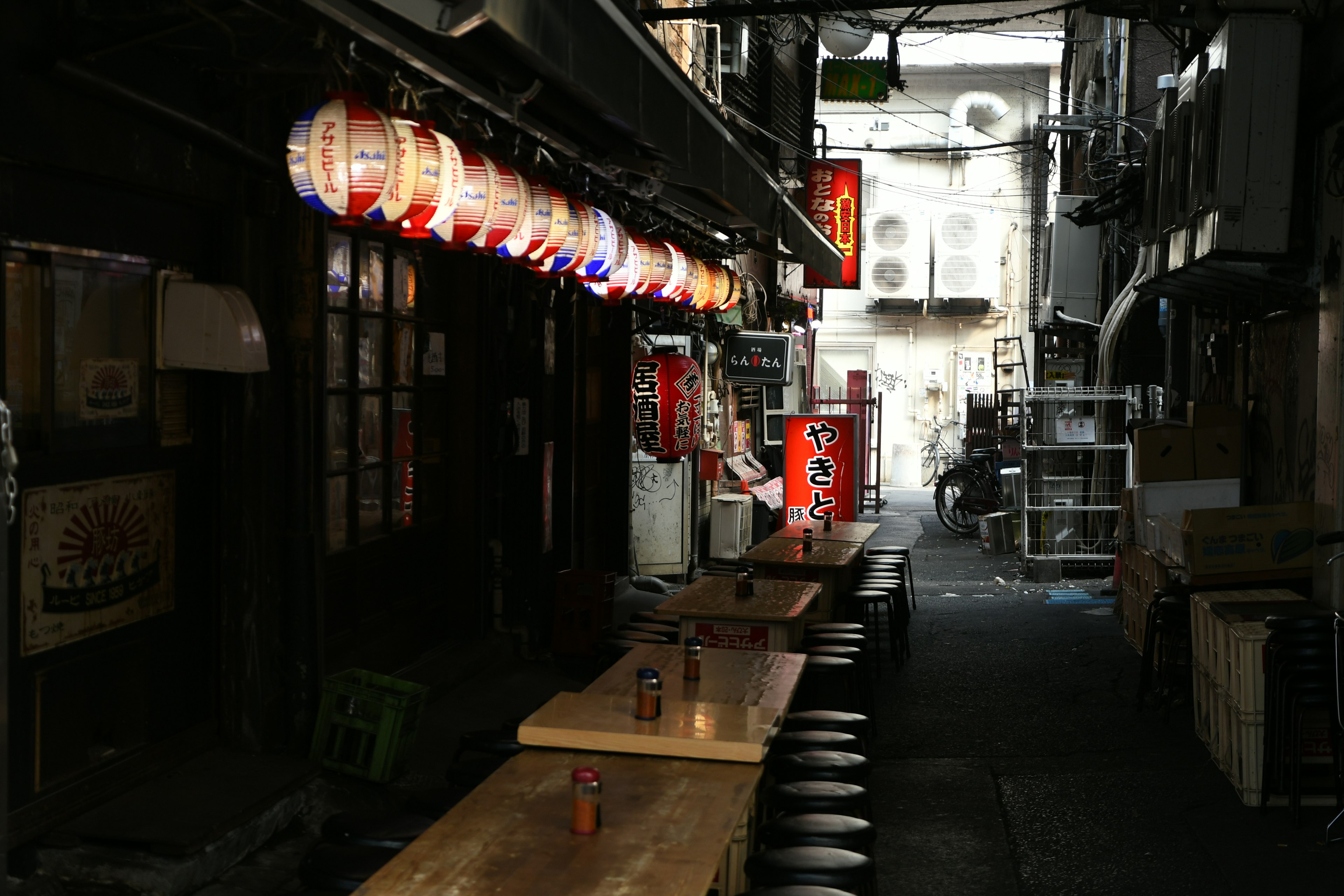 Schmaler Gang mit hängenden Laternen und Holztischen in einem japanischen Izakaya