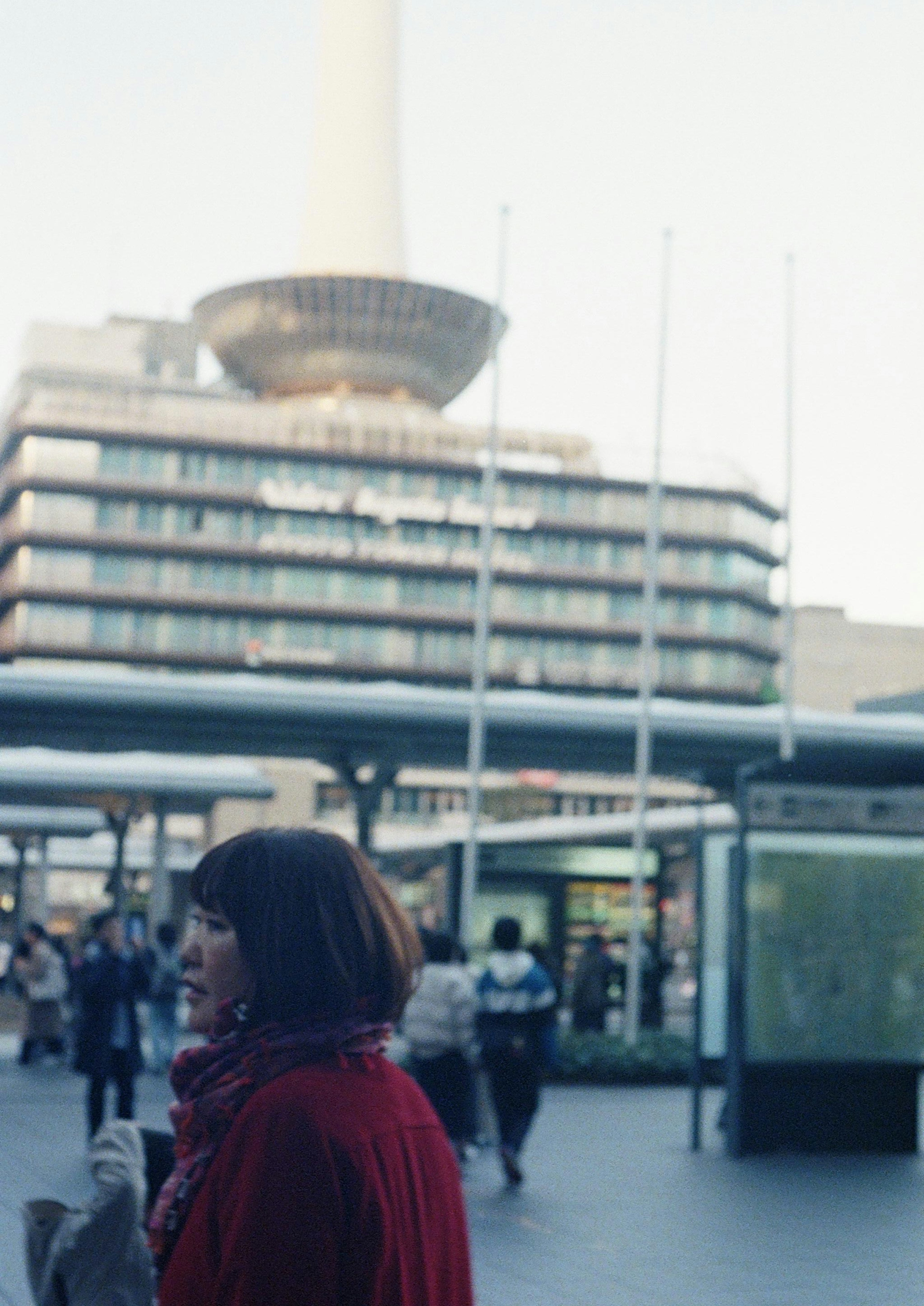 Une femme en manteau rouge marchant dans une place de la ville avec un bâtiment moderne en arrière-plan