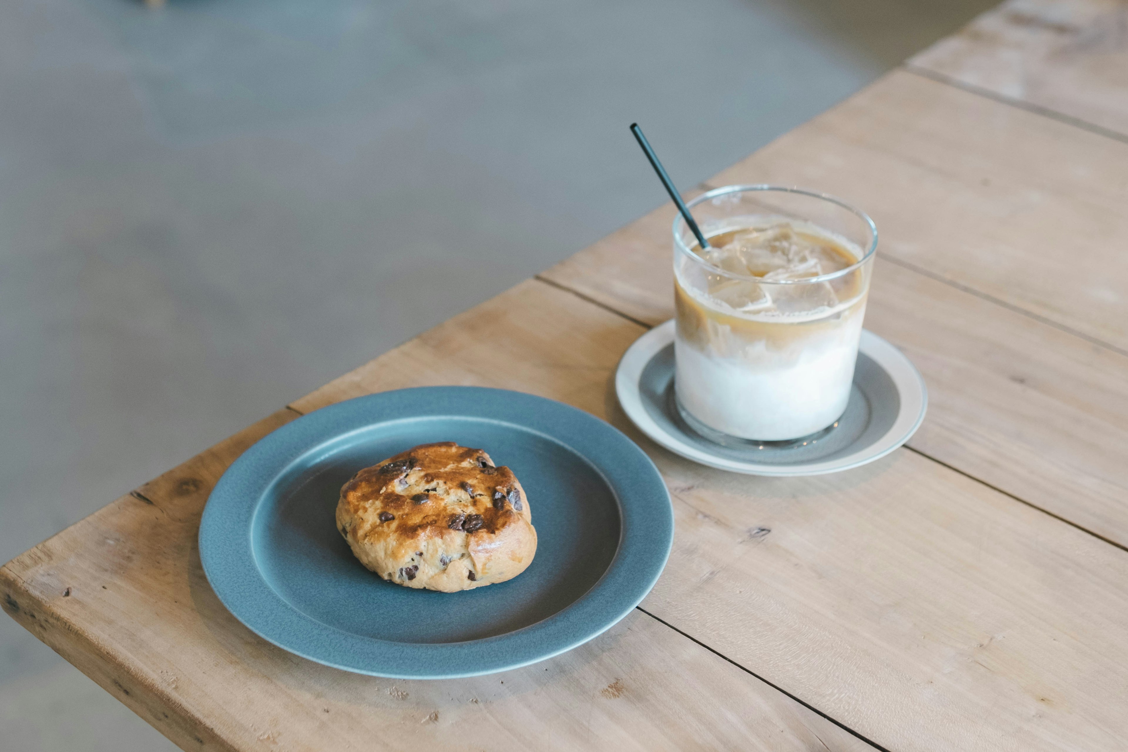 A cookie on a blue plate next to a glass of iced coffee on a wooden table