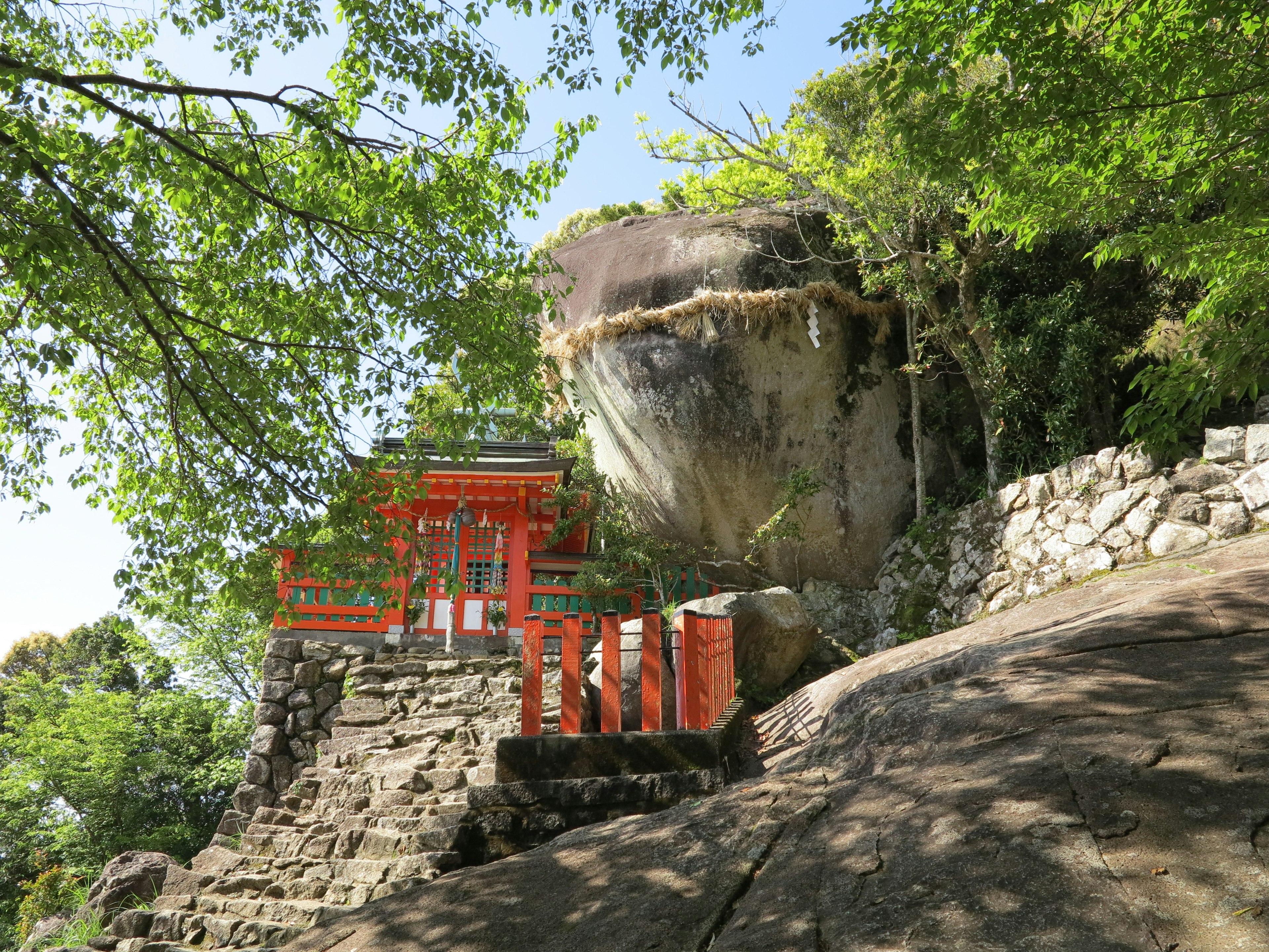 被綠色樹木環繞的神社景觀，帶有紅色鳥居和大岩石