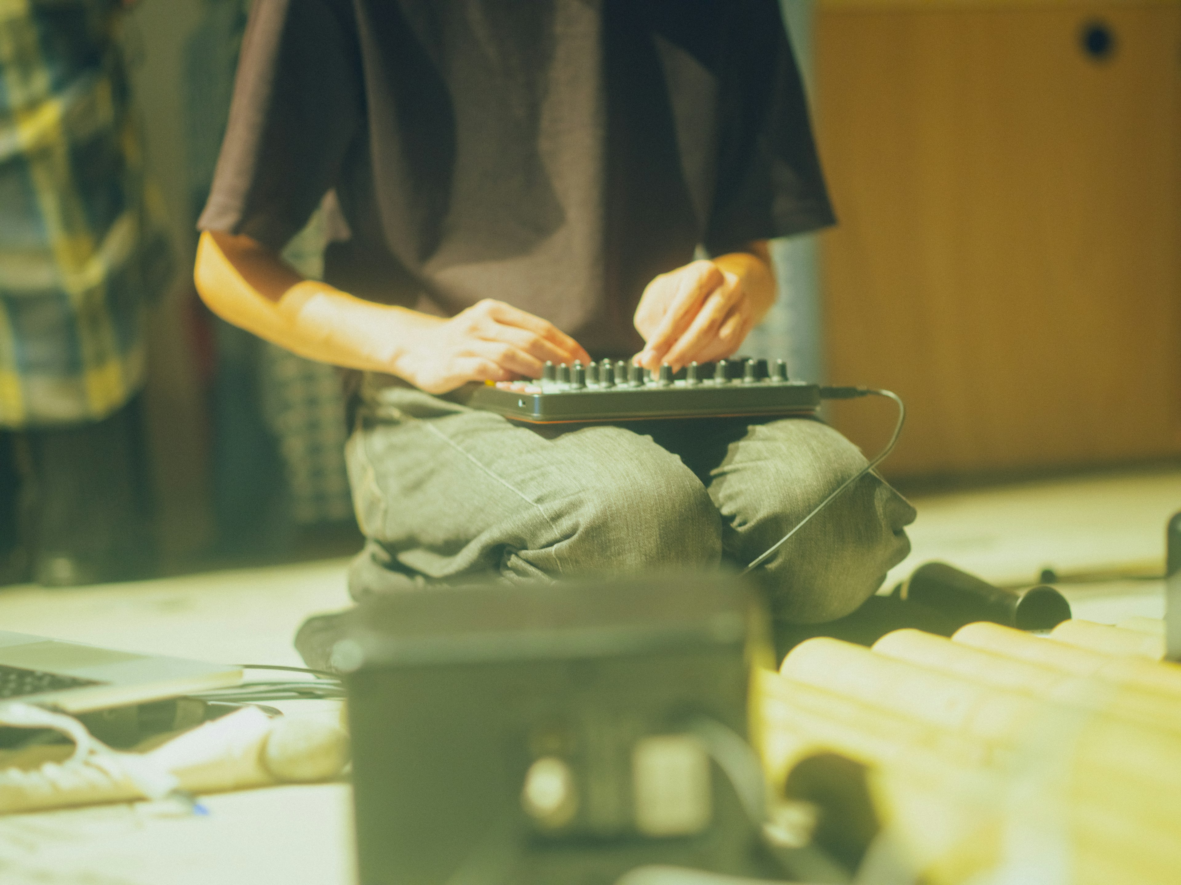 Person playing a synthesizer on the floor with a casual outfit