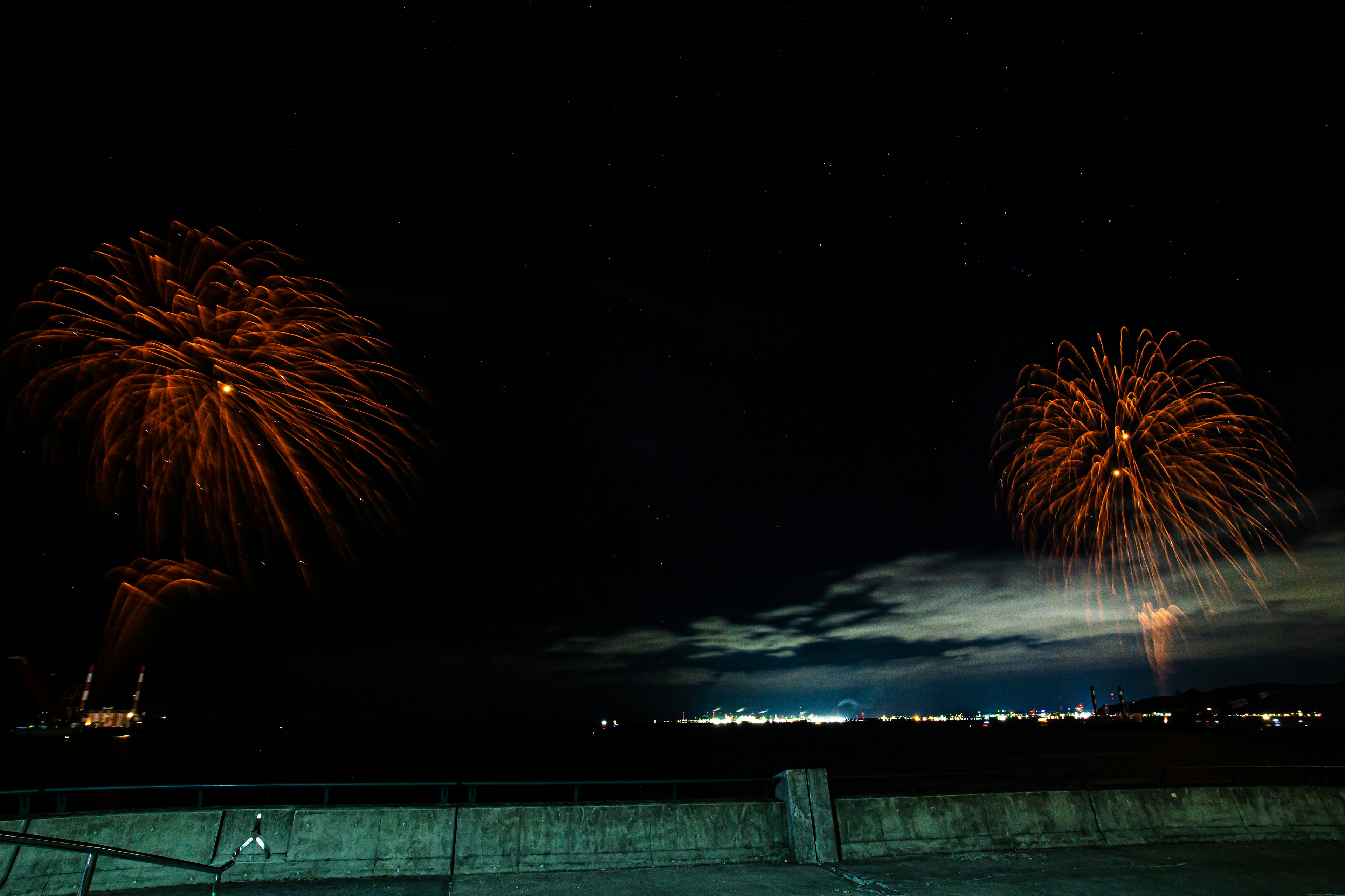 夜空に輝くオレンジ色の花火が二つ上がっている海辺の風景