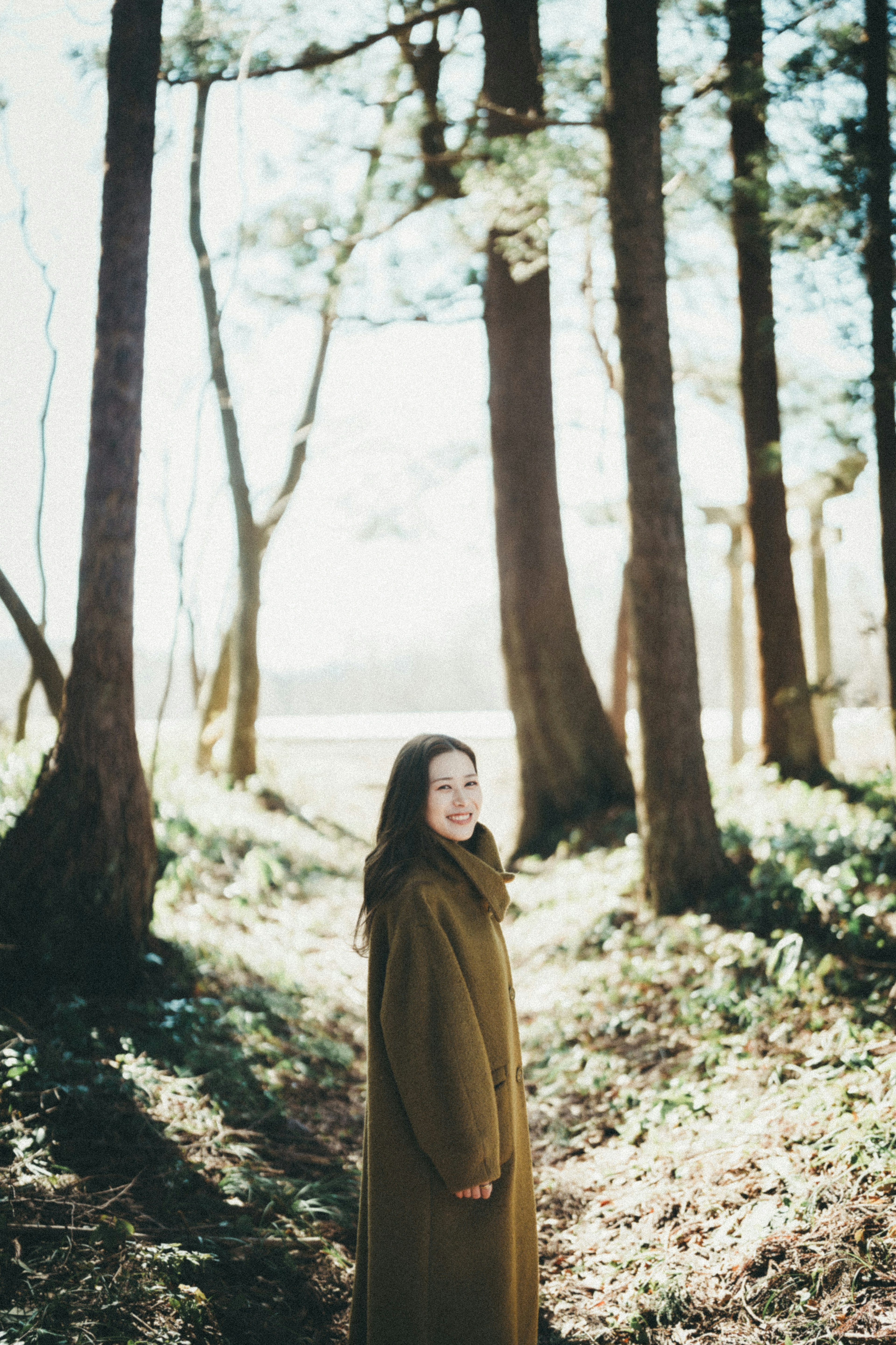 Donna in piedi su un sentiero nel bosco con la luce del sole che filtra tra gli alberi