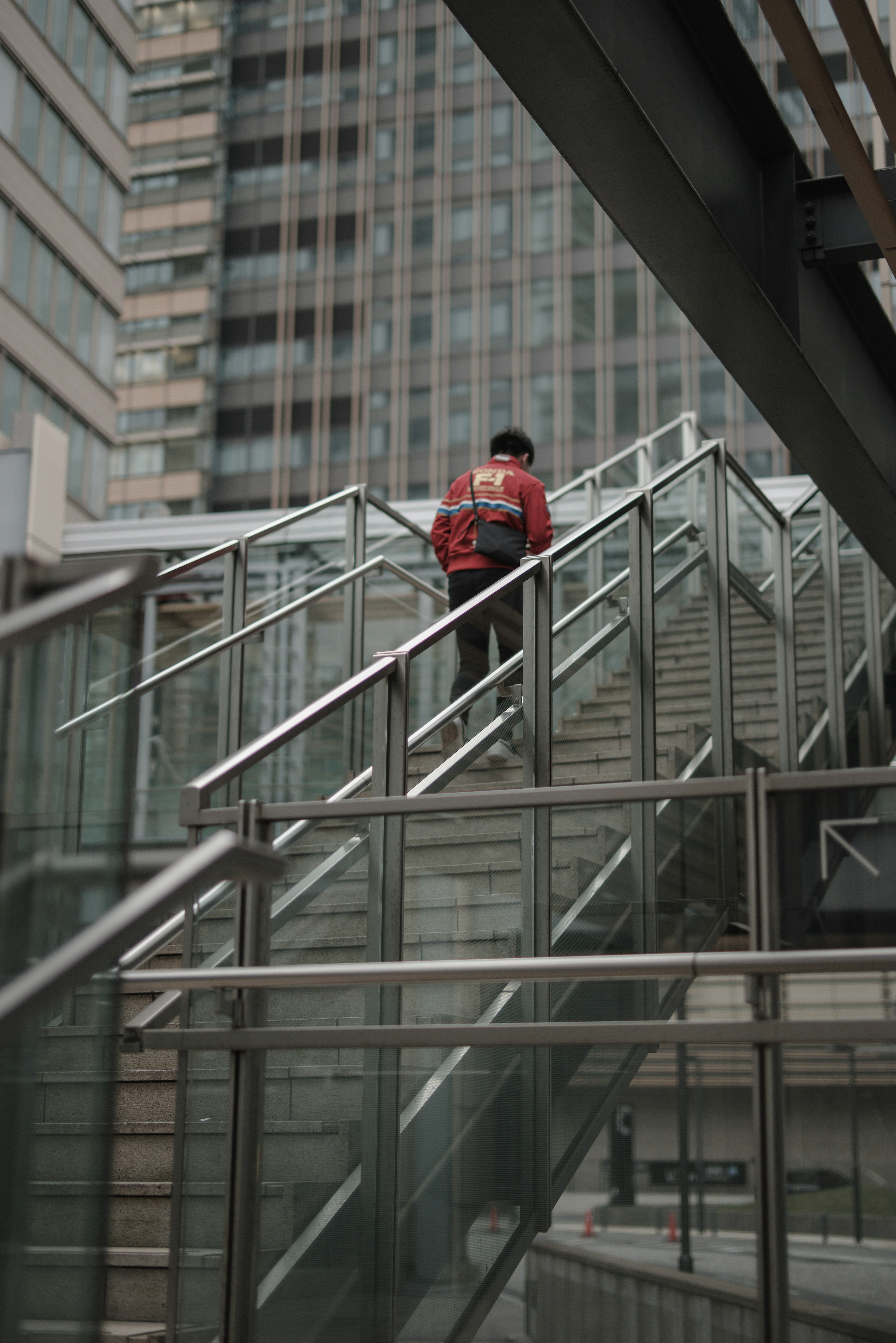 Personne en vêtements rouges montant un escalier avec des rampes en verre et en métal