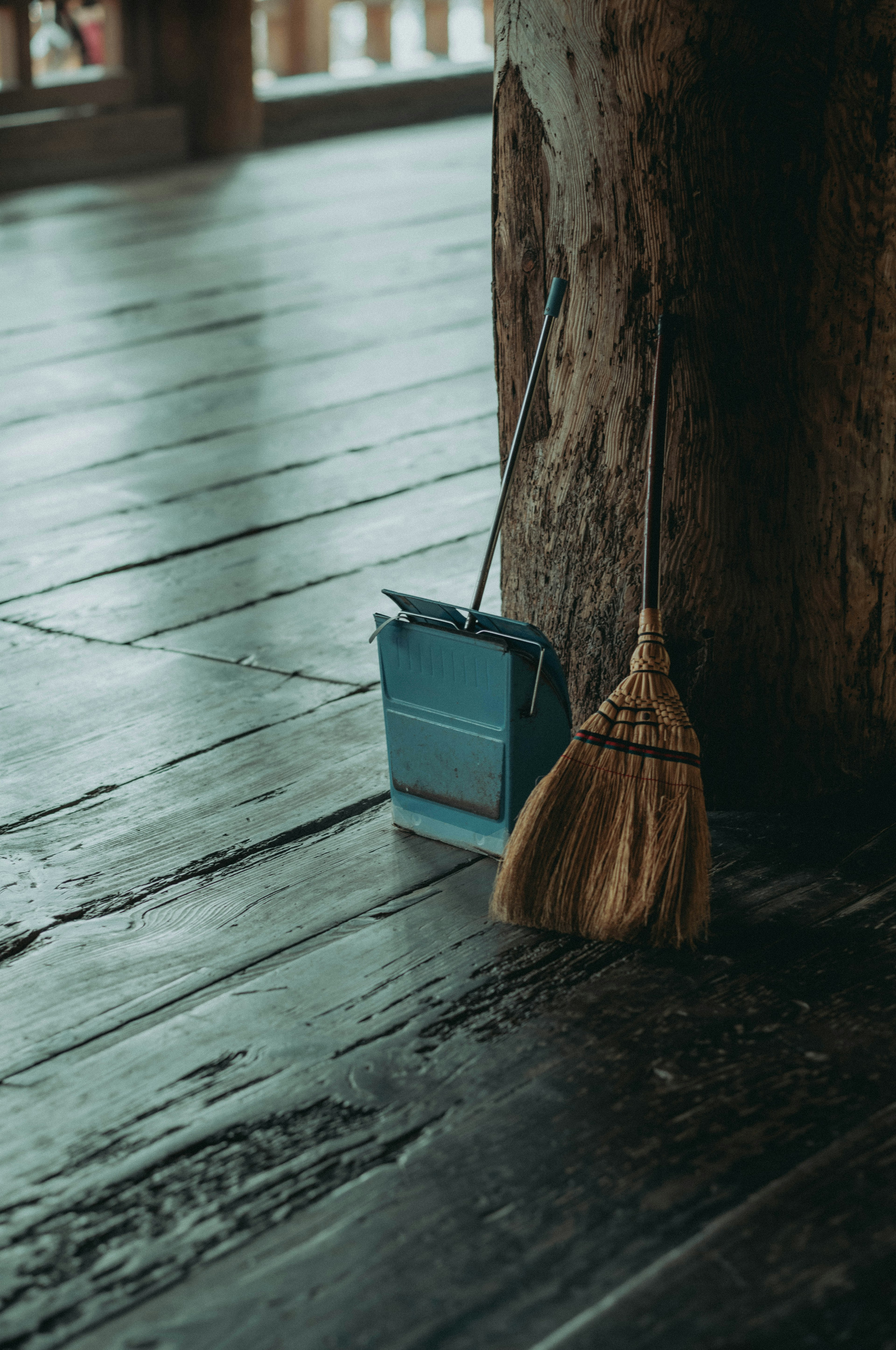 Eine blaue Kehrschaufel und ein Besen stehen neben einem Holzpfosten