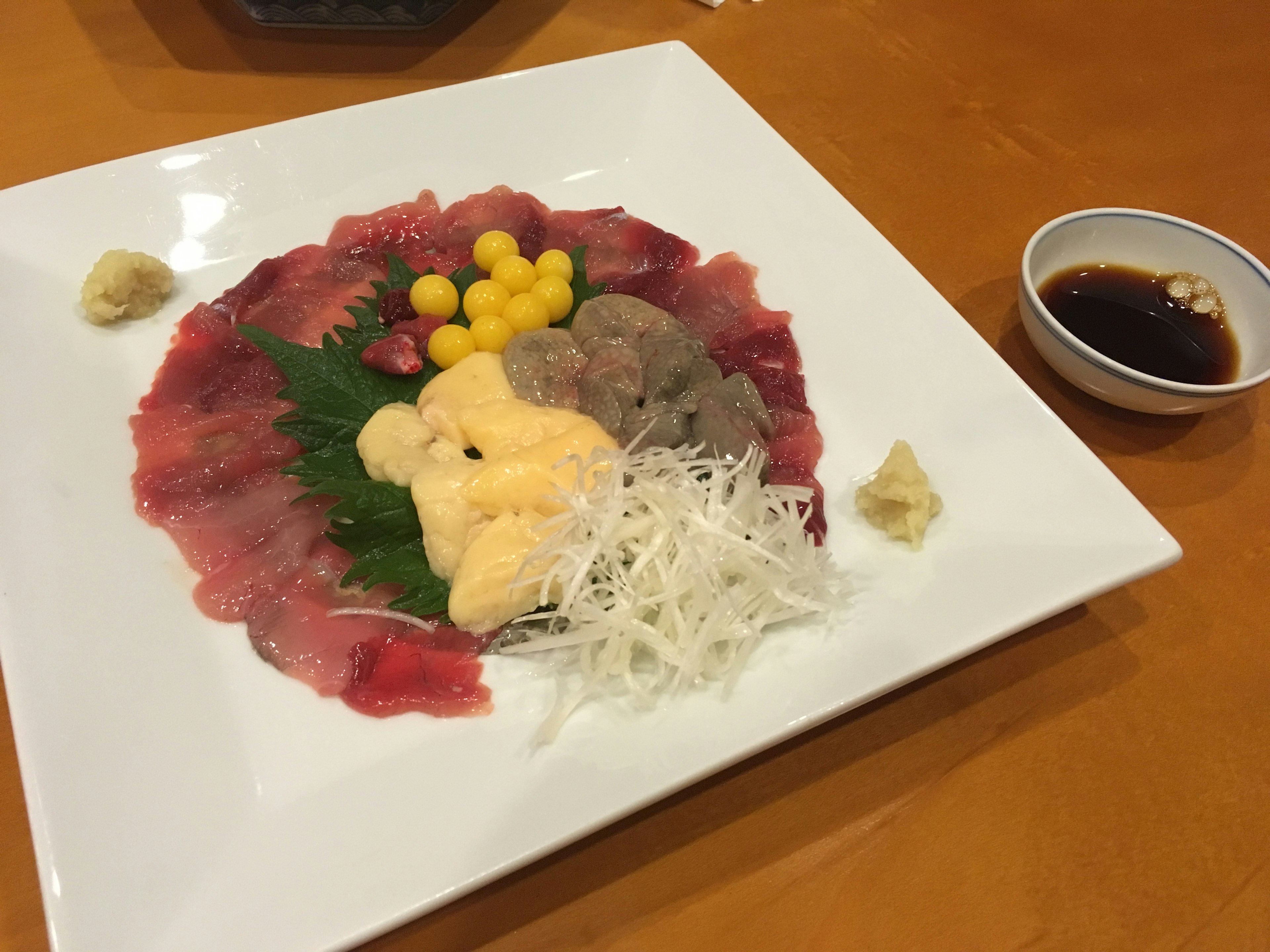 Hermoso plato de sashimi con varias rodajas de pescado y huevas amarillas servido con salsa de soja y wasabi