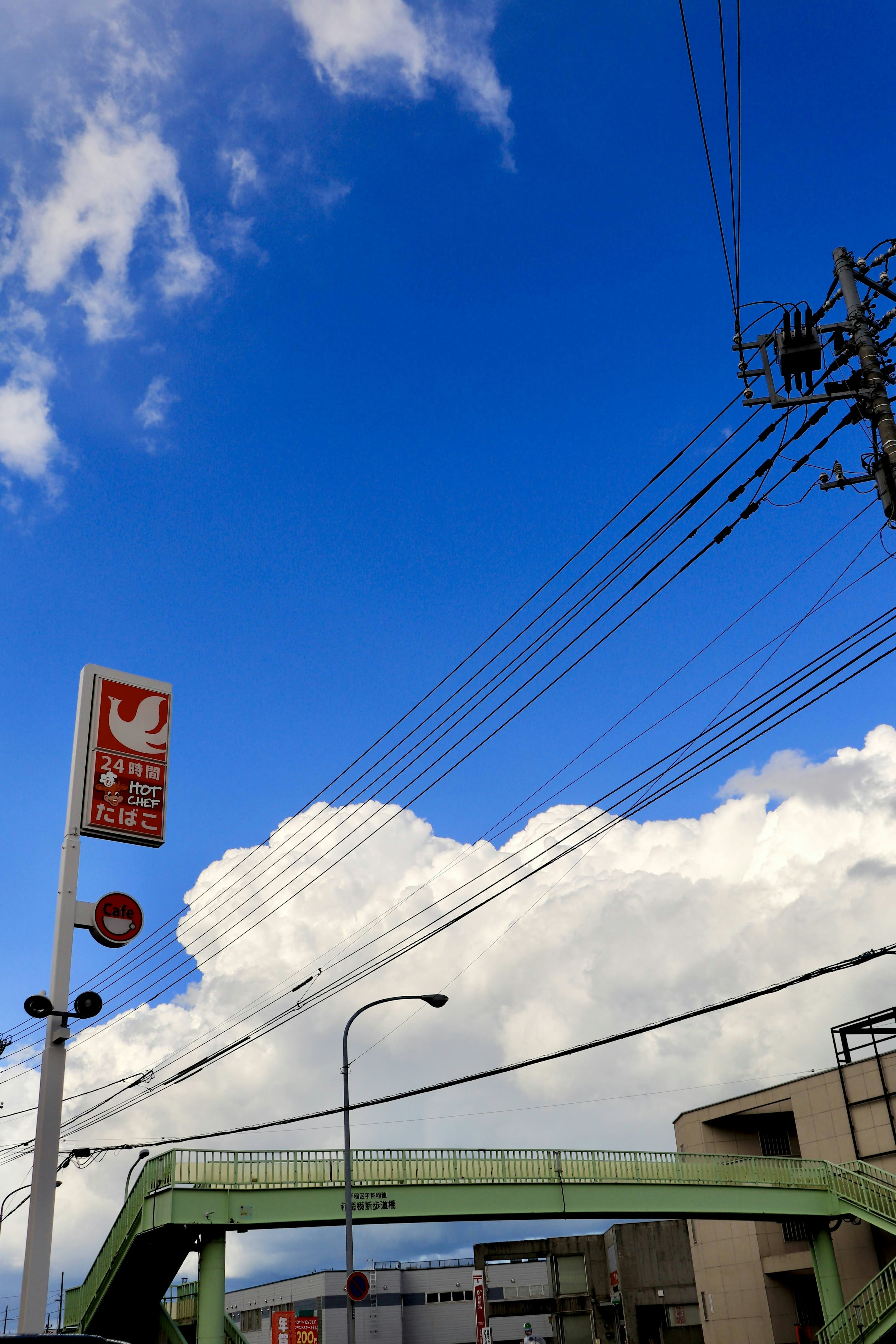 Ciel bleu clair avec des nuages blancs duveteux pont piéton vert et lignes électriques