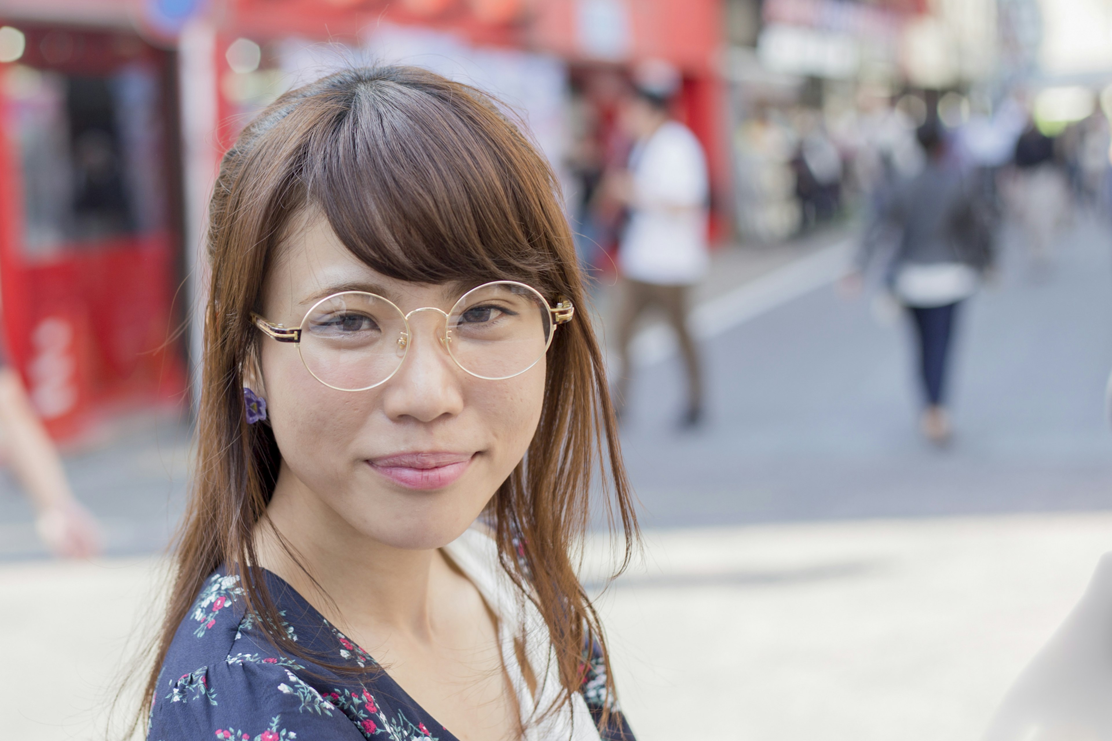 Eine Frau mit Brille lächelt in einer belebten Straßenszene