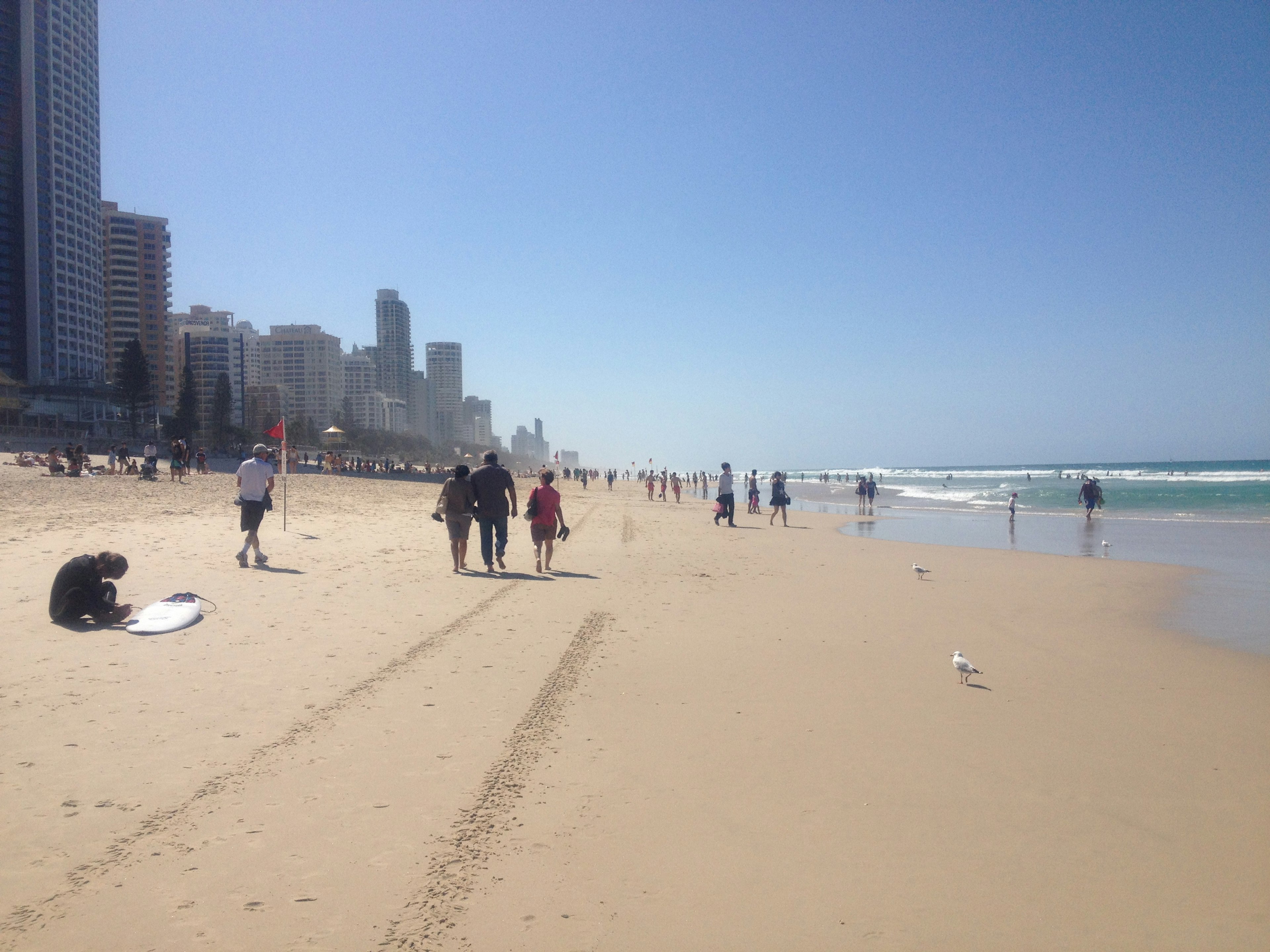 Personas caminando por la playa con edificios altos al fondo