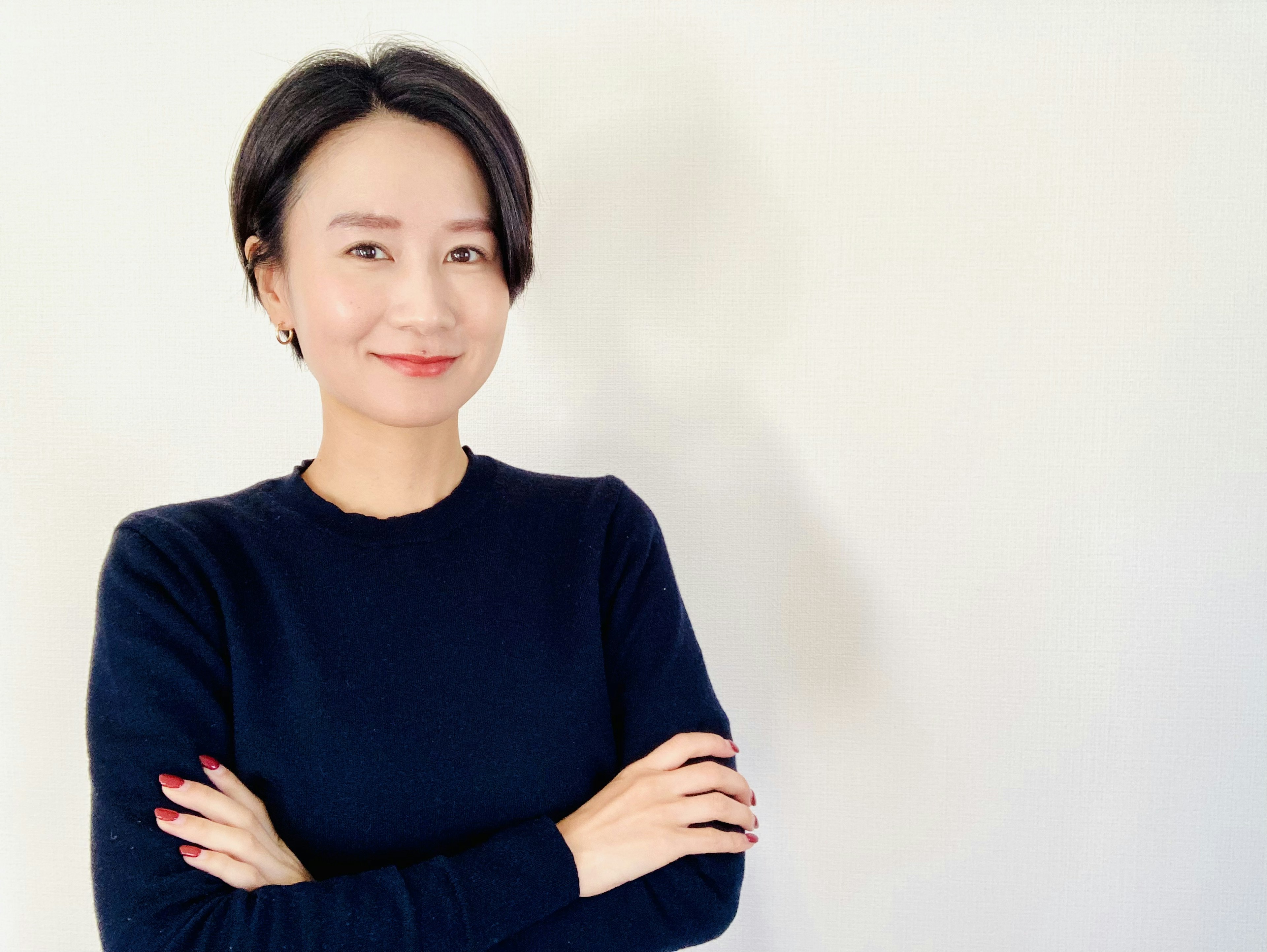 Woman smiling with arms crossed in front of a white background