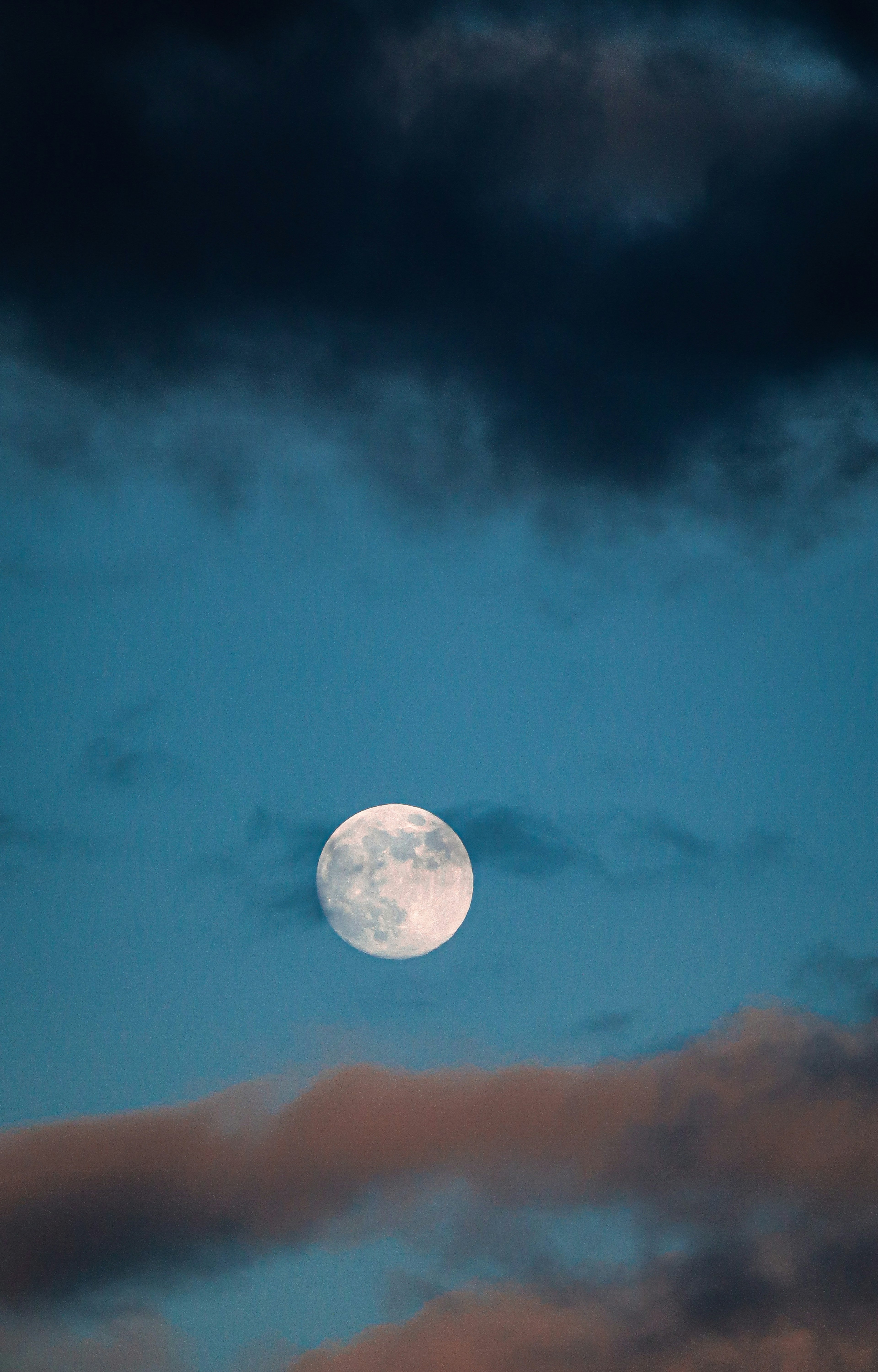 Full moon floating in a blue sky with contrasting clouds