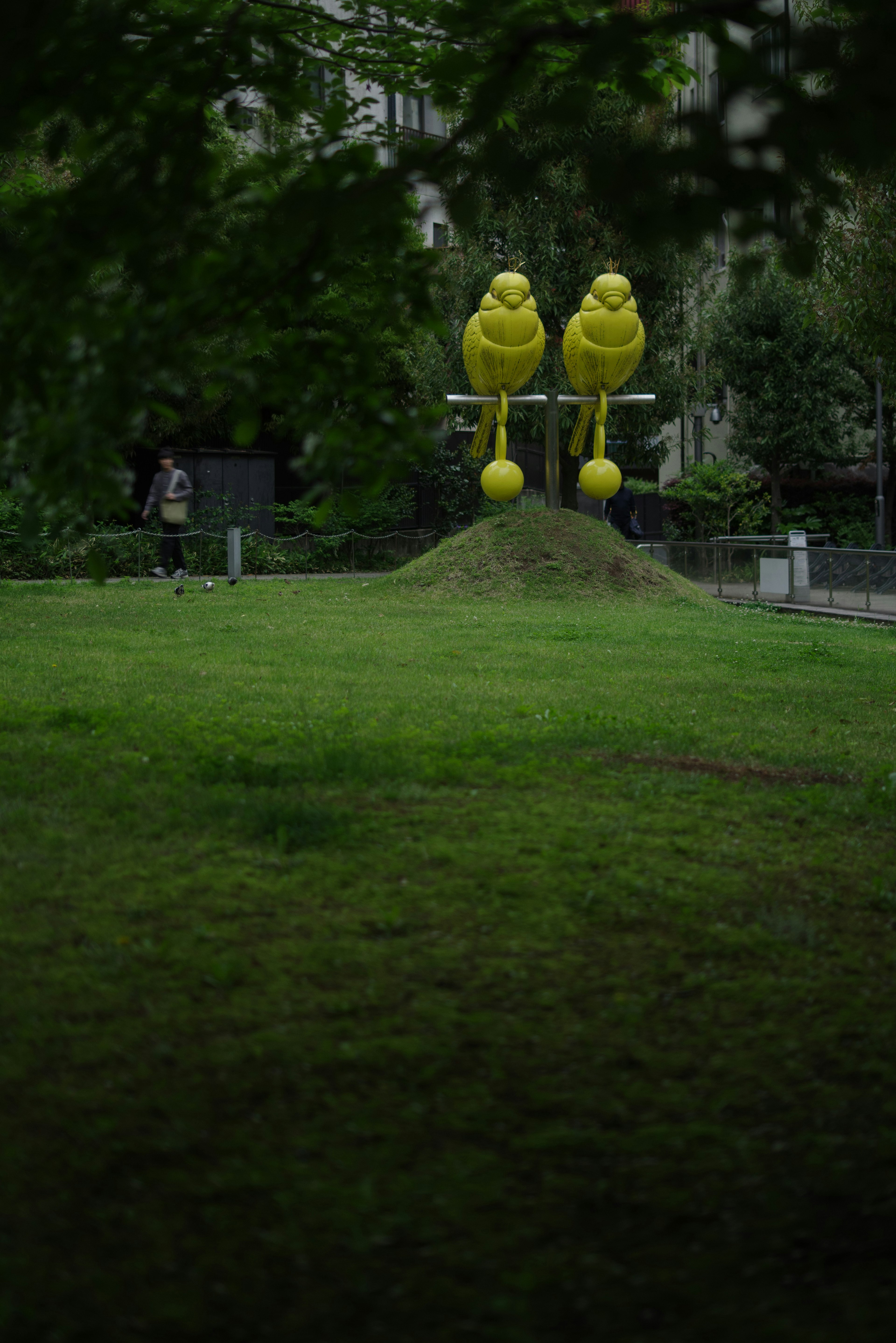 Two yellow bird sculptures are standing on a grassy area