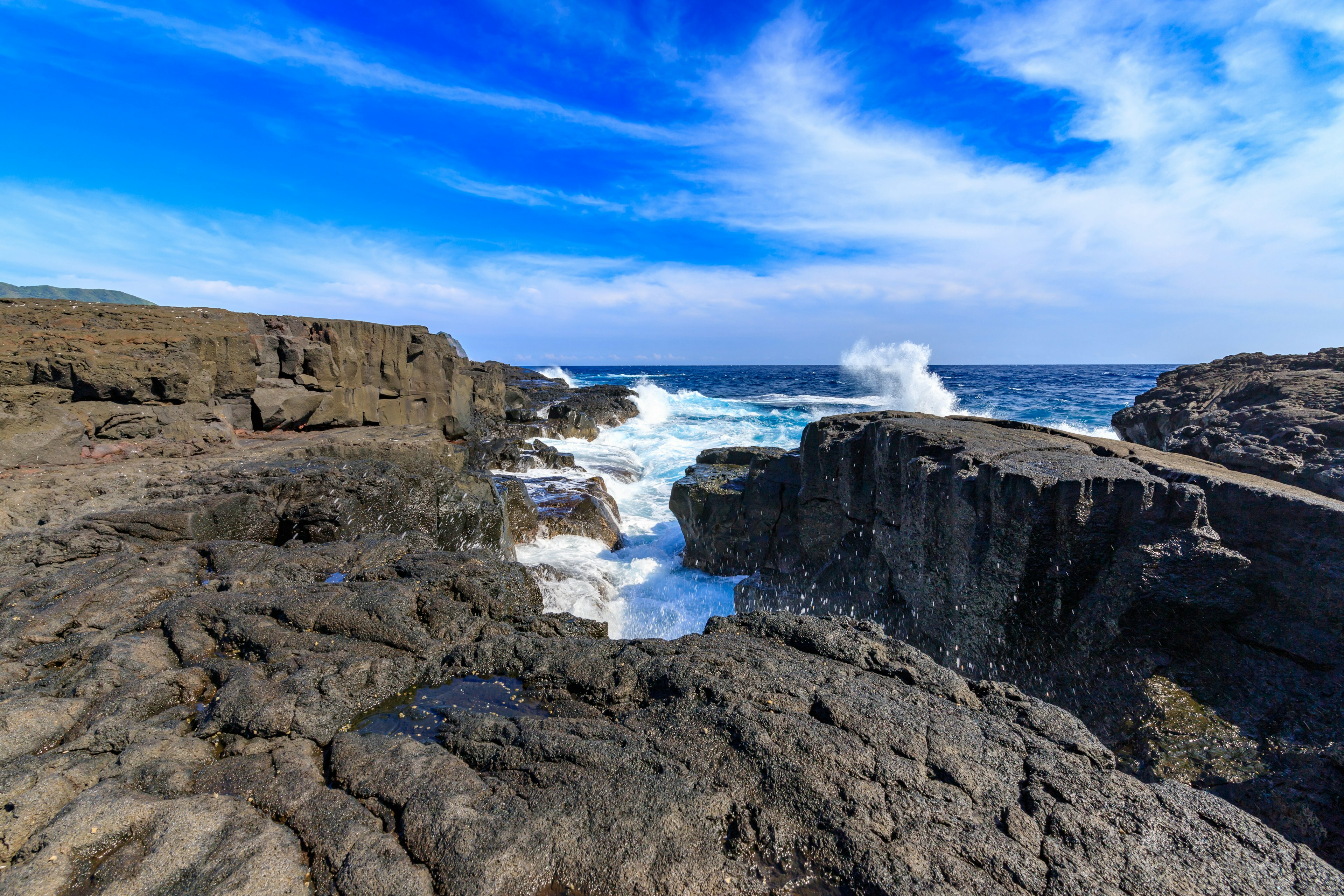 Escena costera con cielo azul y olas rompiendo en la costa rocosa