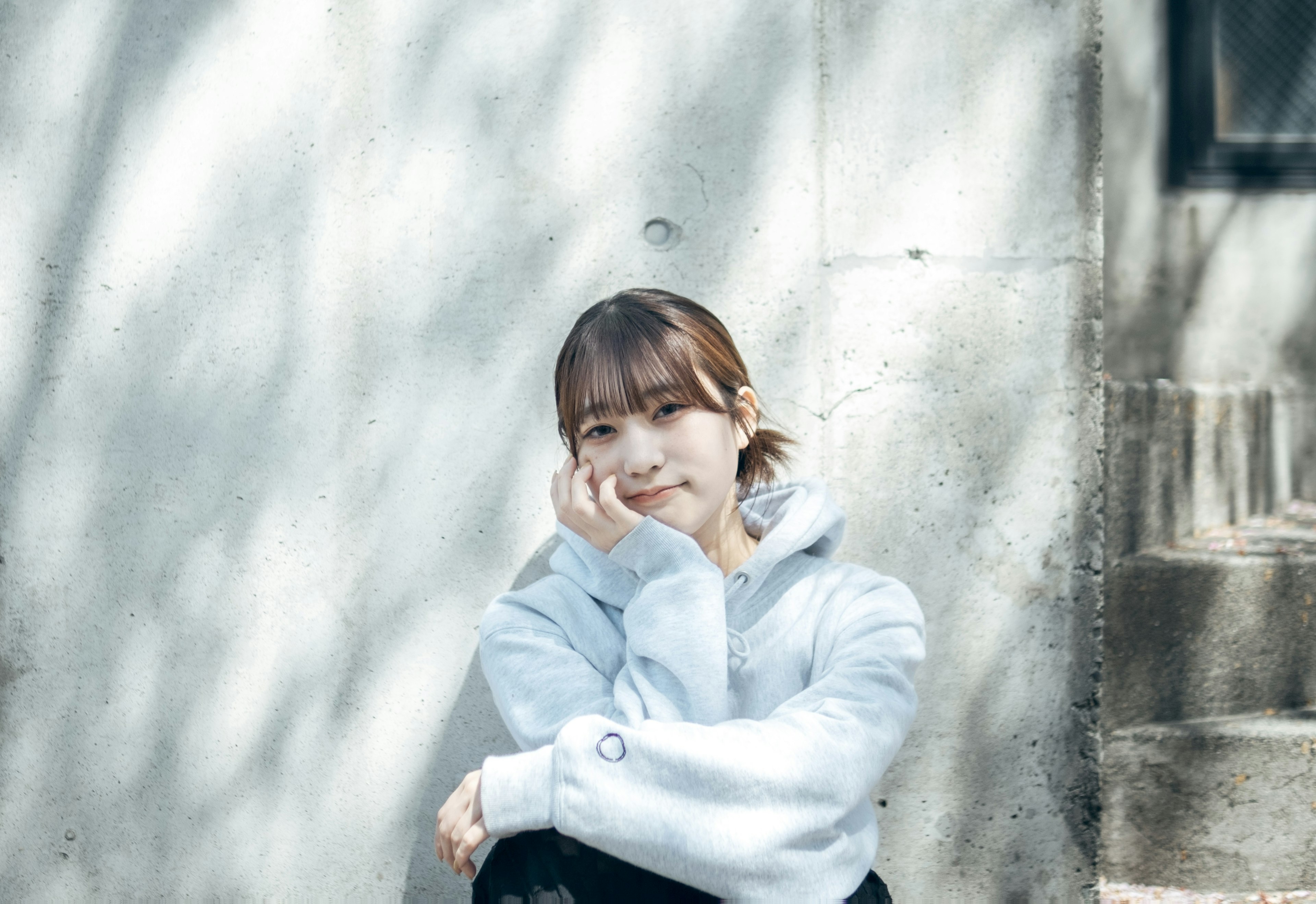 A young woman sitting in front of a wall lost in thought with natural light casting shadows