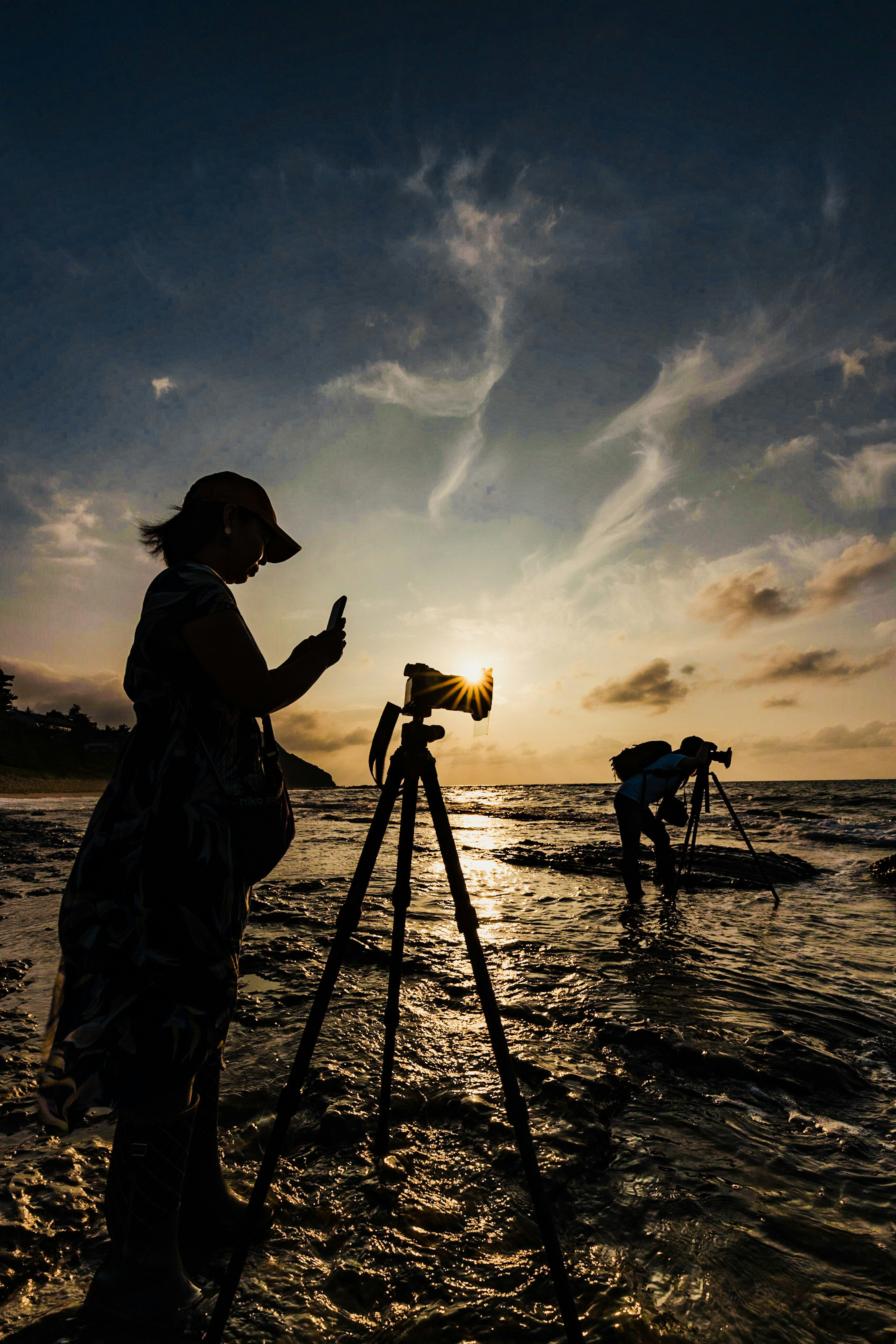 Siluet fotografer dengan tripod di pantai saat matahari terbenam