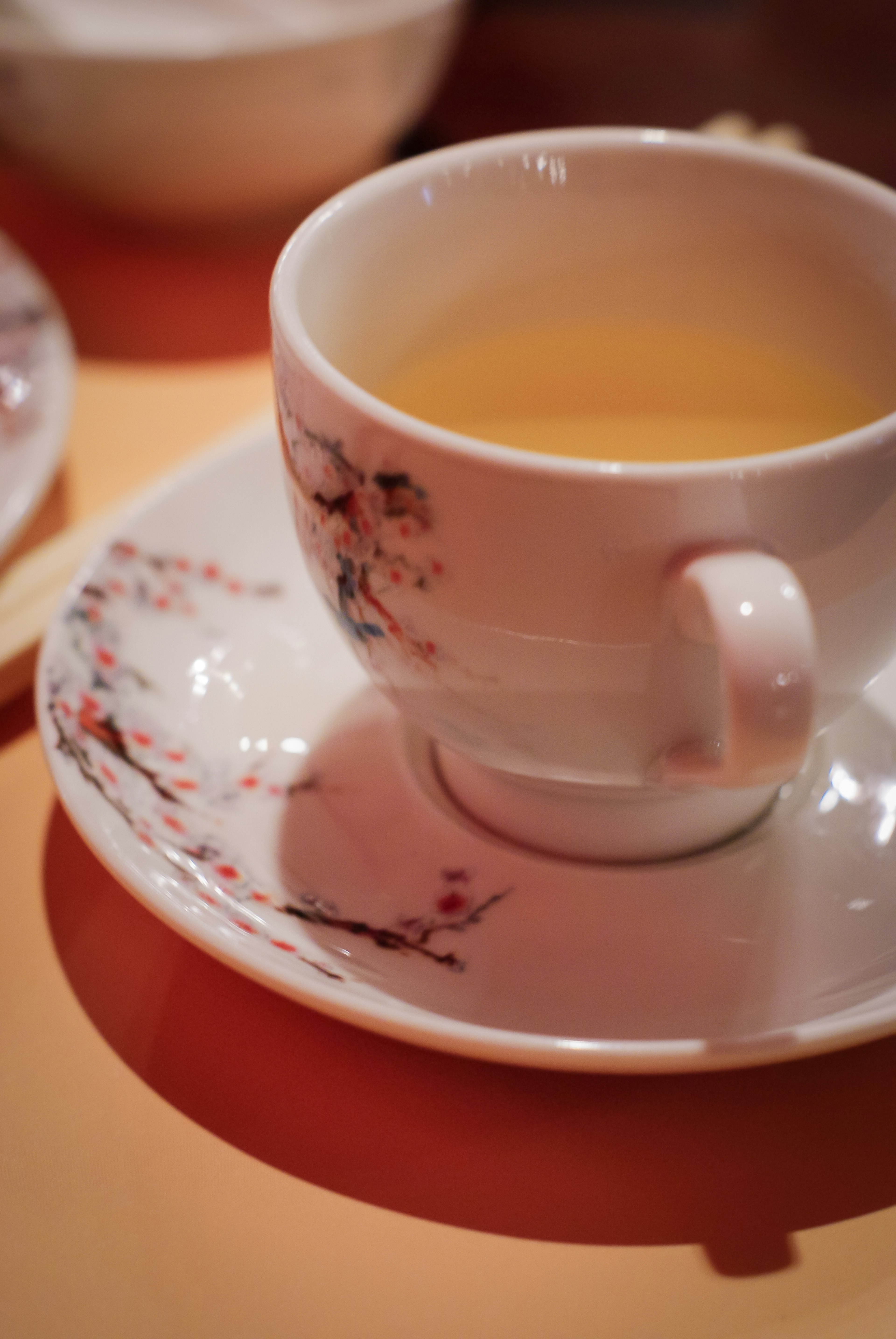 Une tasse de thé avec un beau motif de fleurs de cerisier remplie de thé jaune sur une soucoupe assortie