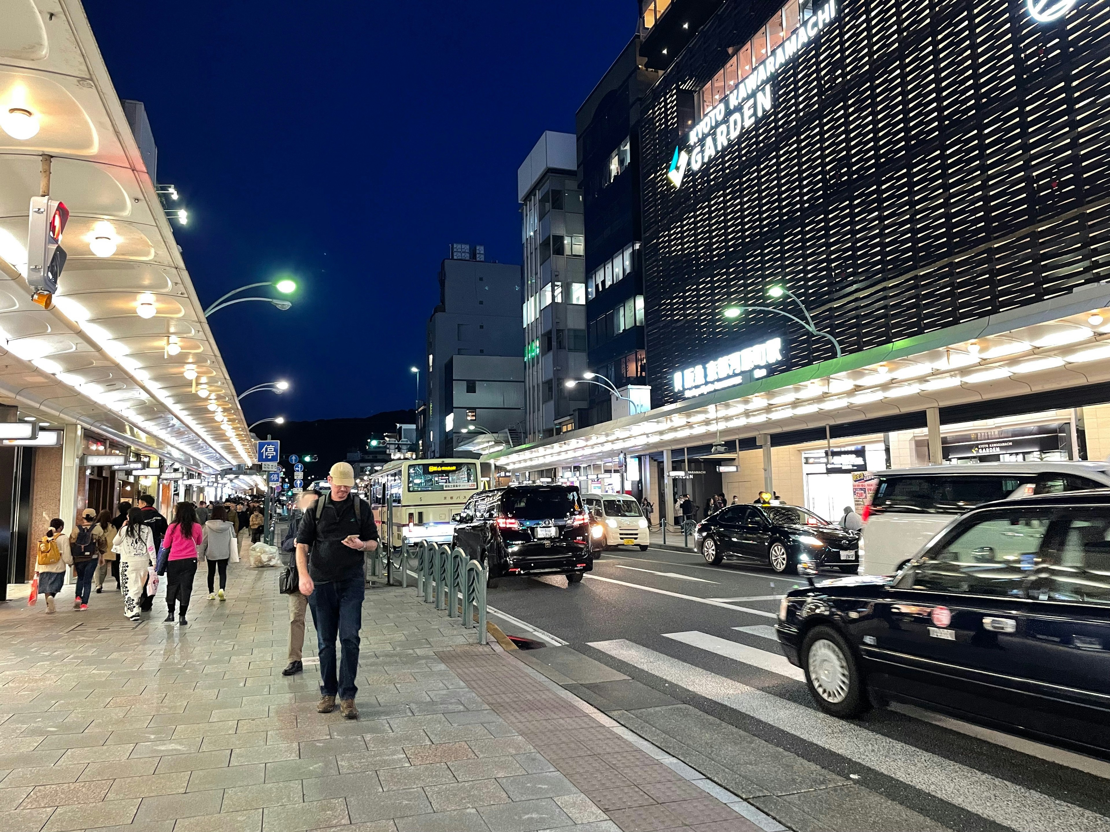 人們在夜晚的城市街道上走，周圍有明亮的標誌