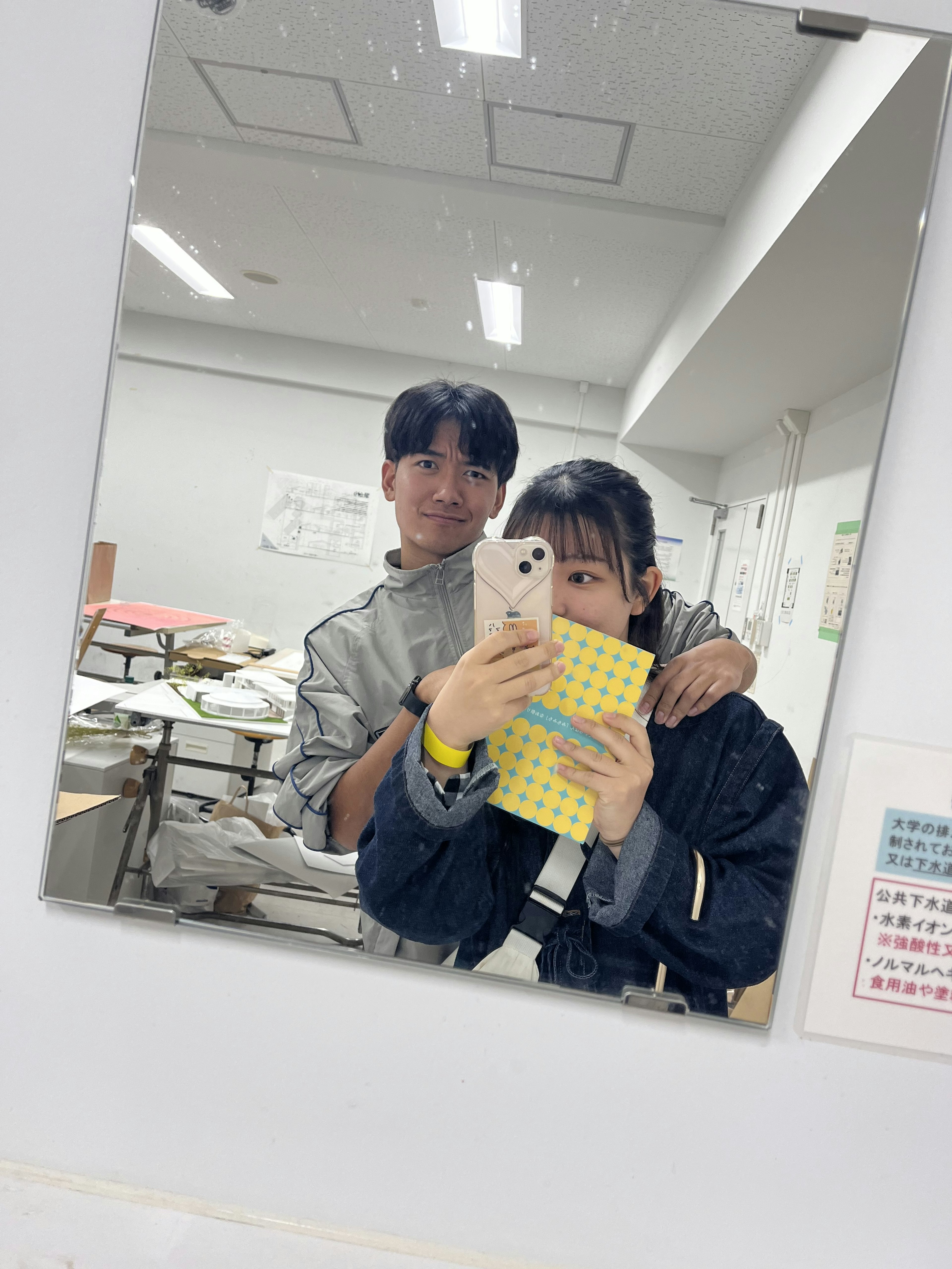 Two young people taking a selfie in a mirror One is wearing a gray outfit and the other is in a black jacket