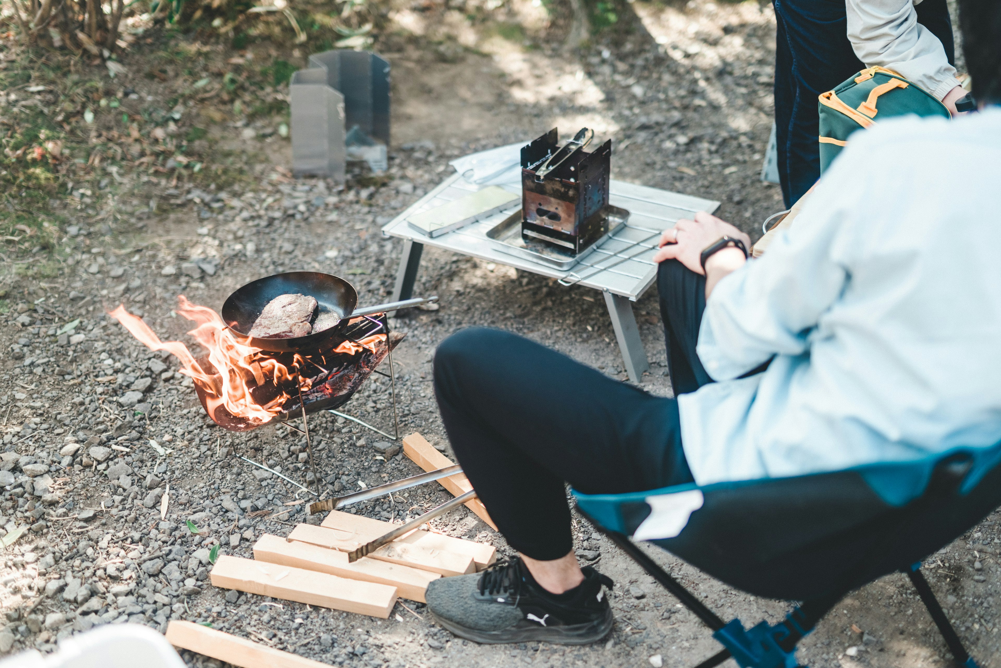 Persona cocinando en un campamento con una estufa portátil y fuego