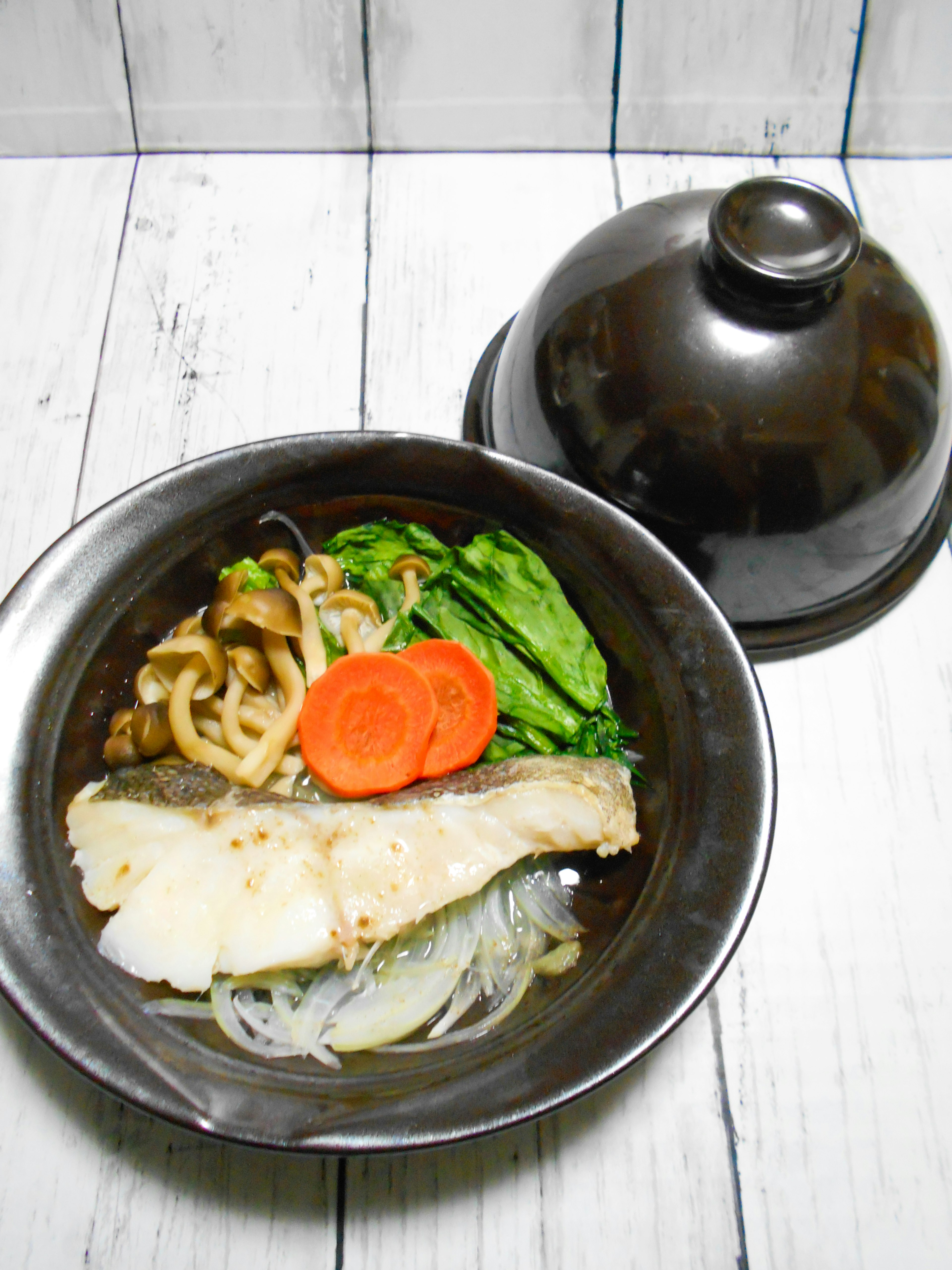 Plato de pescado blanco y verduras servido en un tazón negro