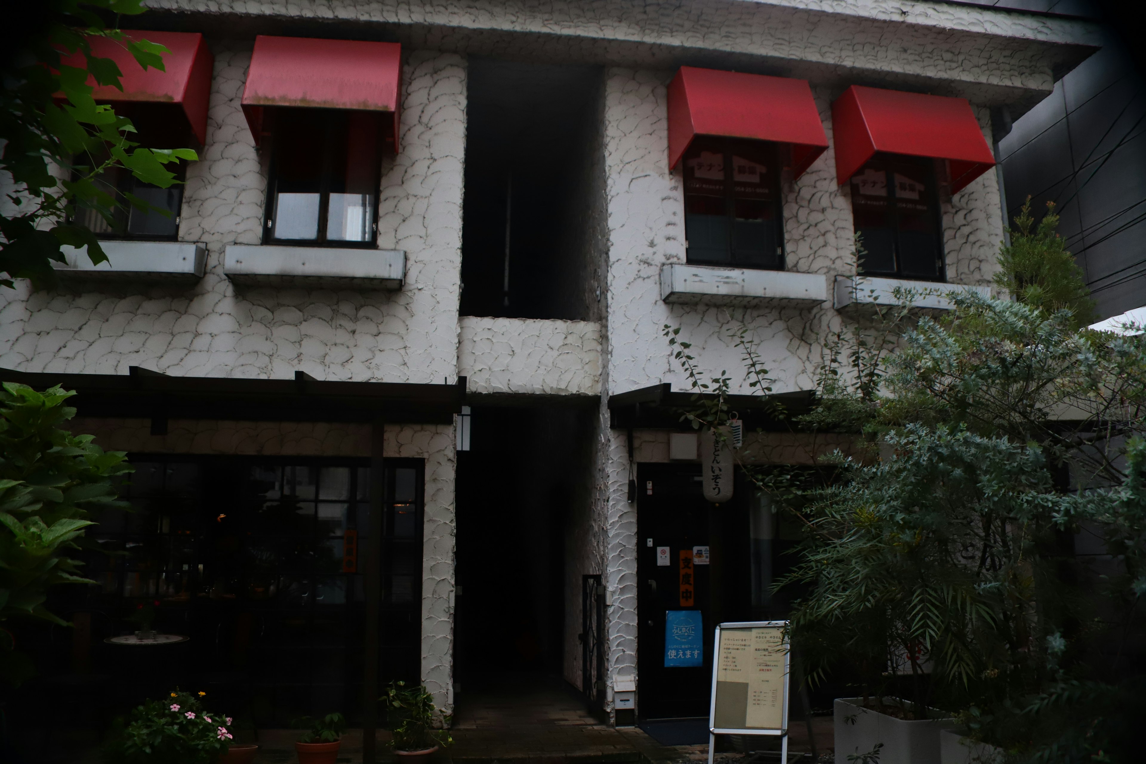 Entrada de un edificio con exterior blanco y ventanas con toldos rojos