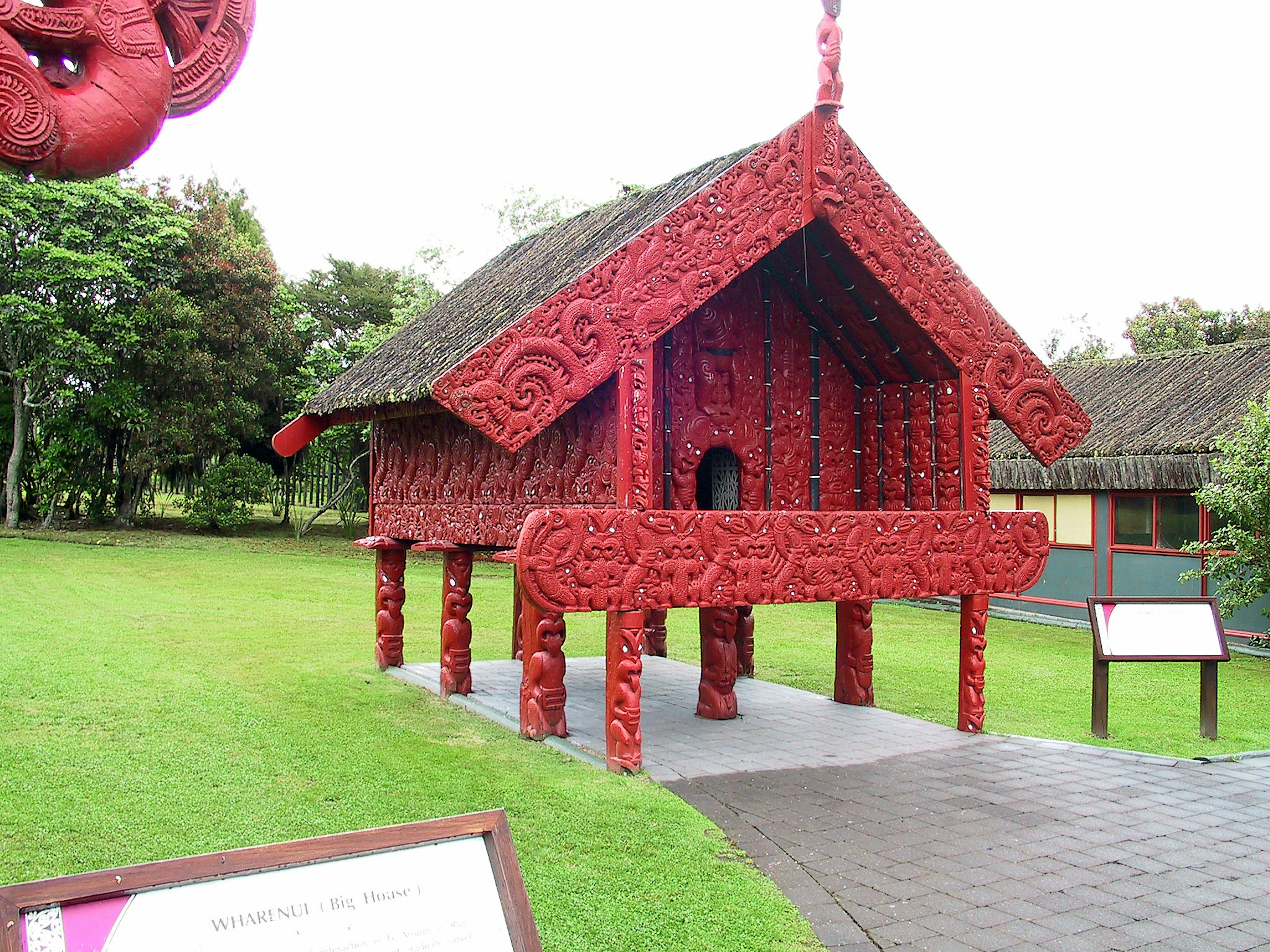 Extérieur d'une maison maorie avec des sculptures rouges complexes entourées d'herbe verte