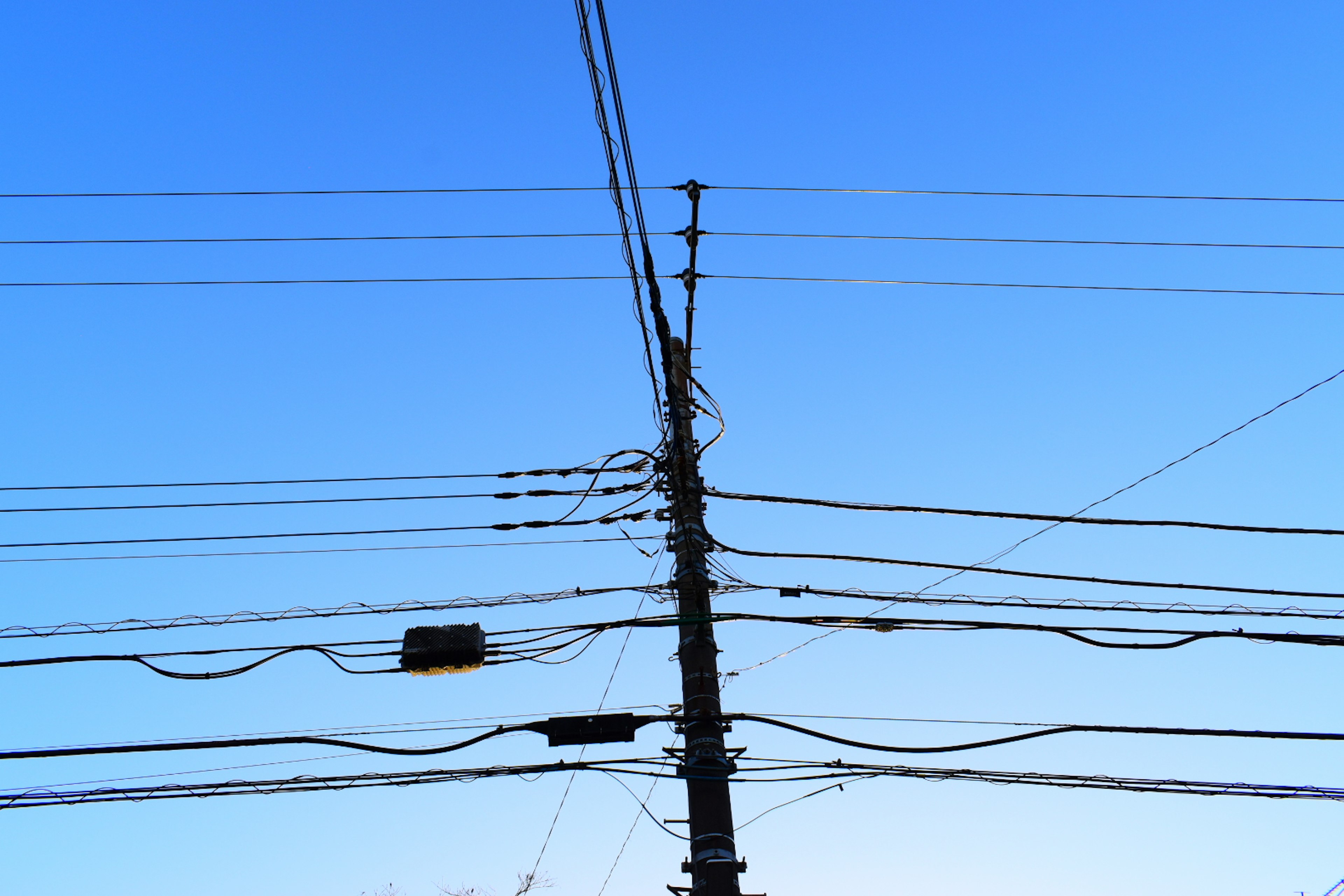 Silhouette von Stromleitungen und Mast vor blauem Himmel