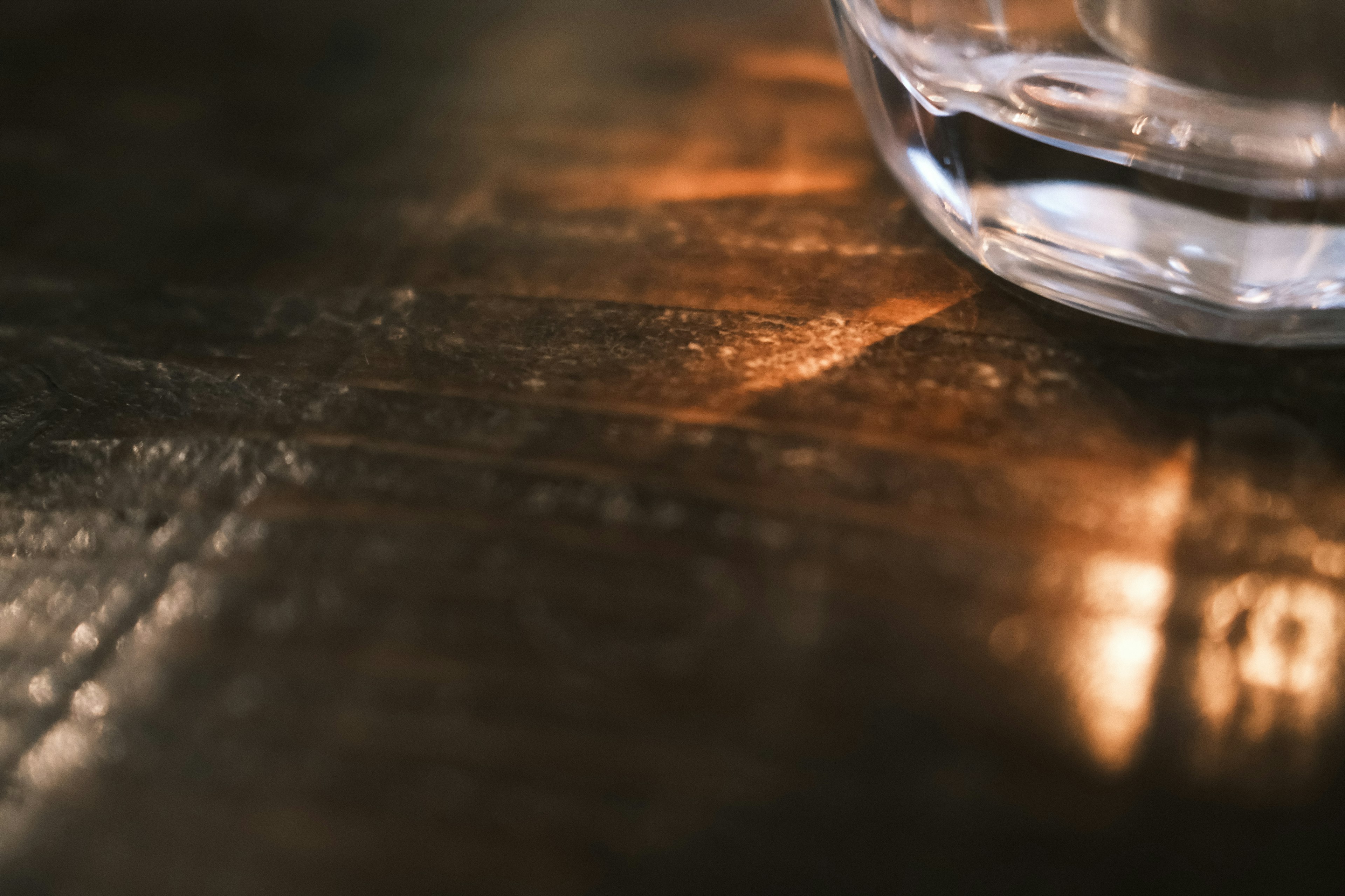 Vista parcial de un vaso transparente sobre una mesa de madera con luz reflejada