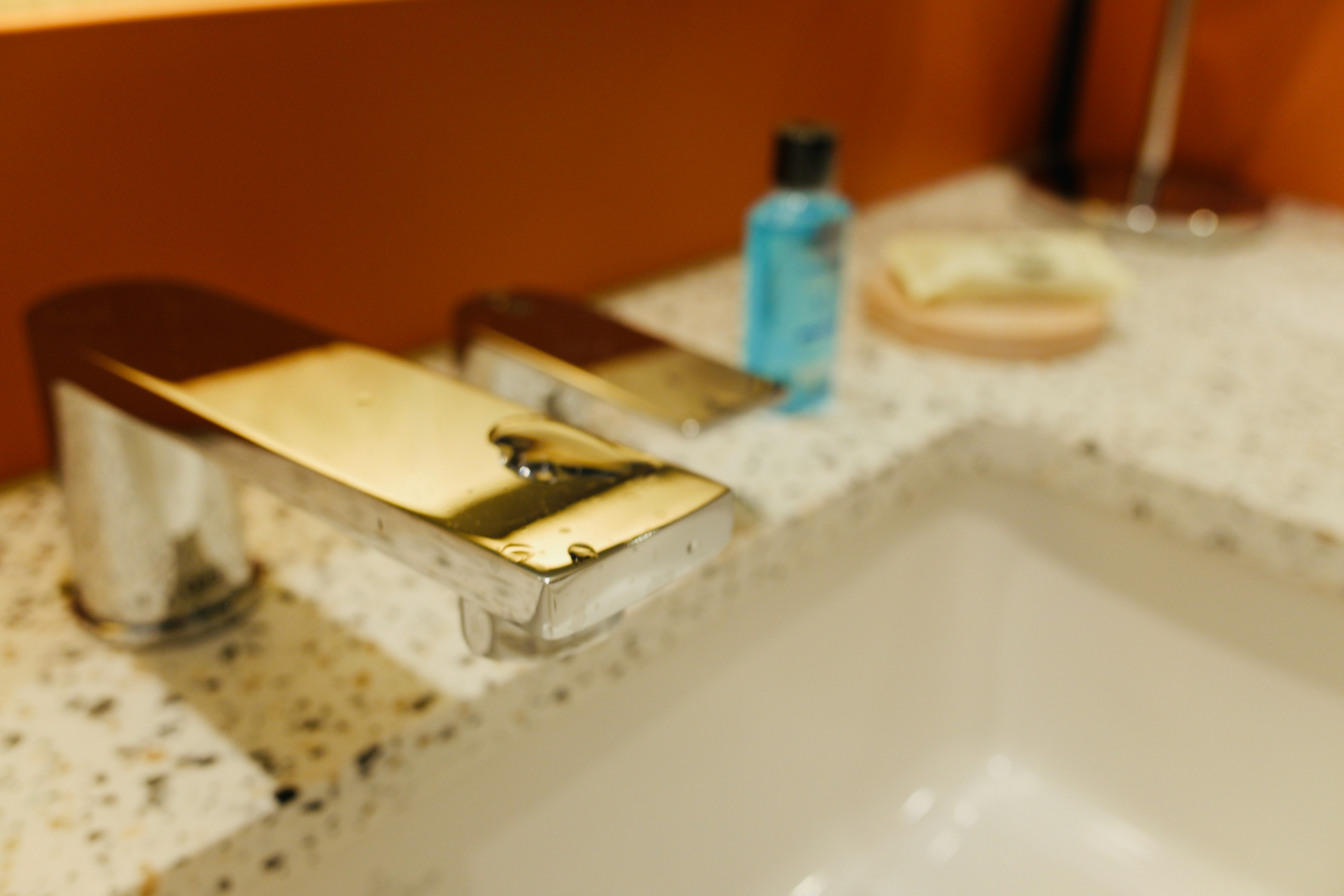 Close-up of a modern faucet and blue bottle on a bathroom countertop