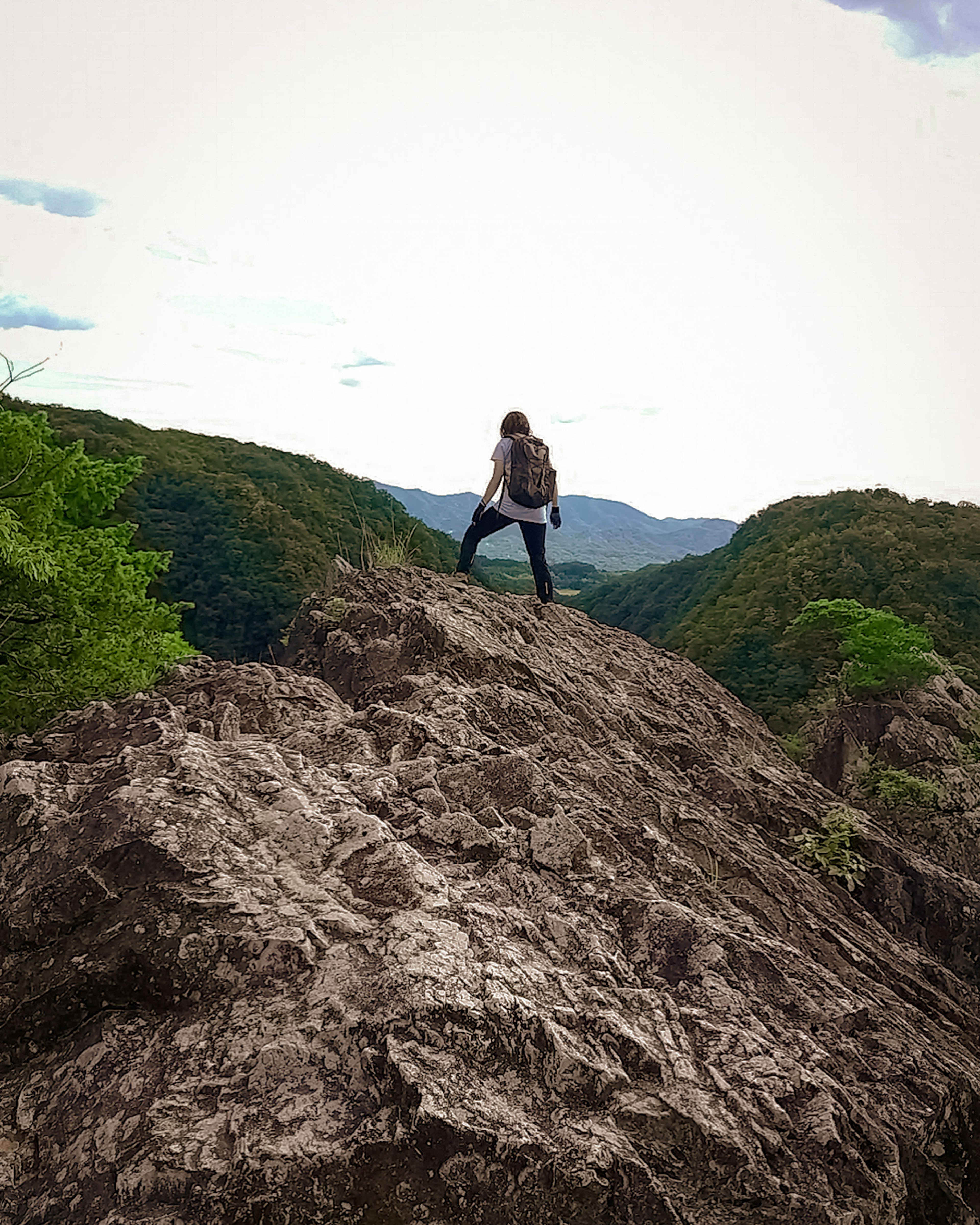 Hiker standing on a rocky summit with green mountains and blue sky in the background