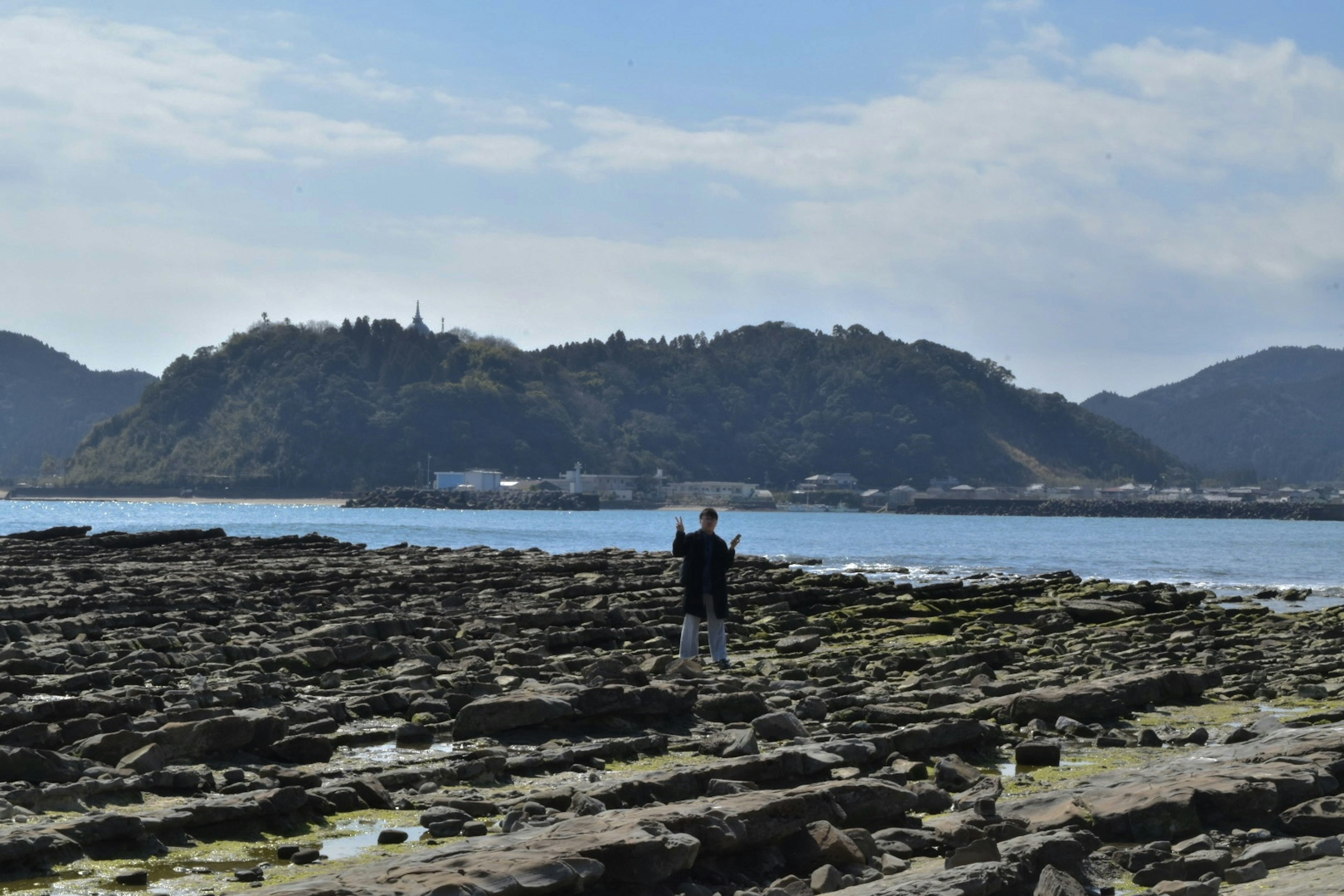 海岸の岩場で立つ人物と山の風景