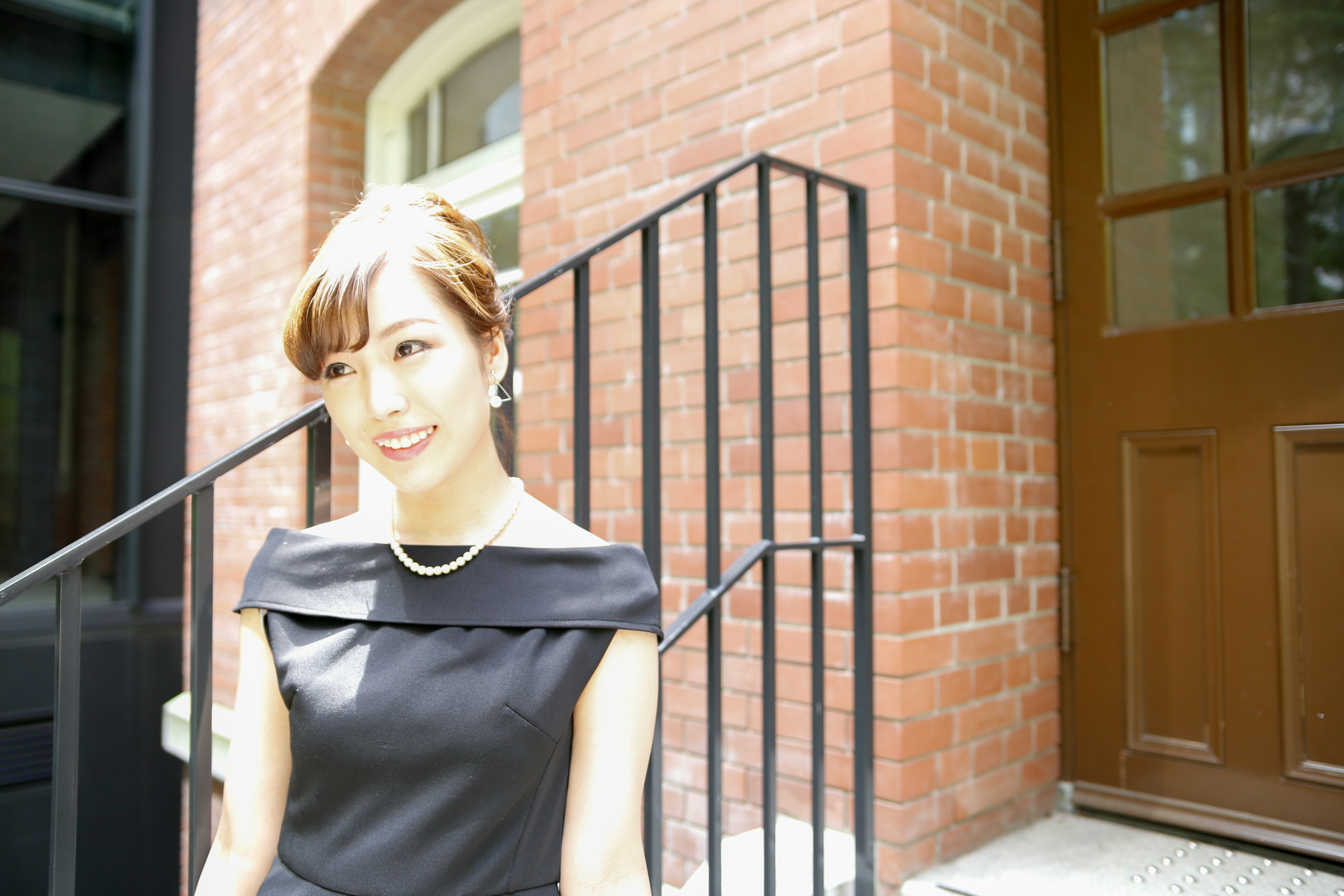 Portrait of a woman standing in front of a brick building wearing a black dress and smiling