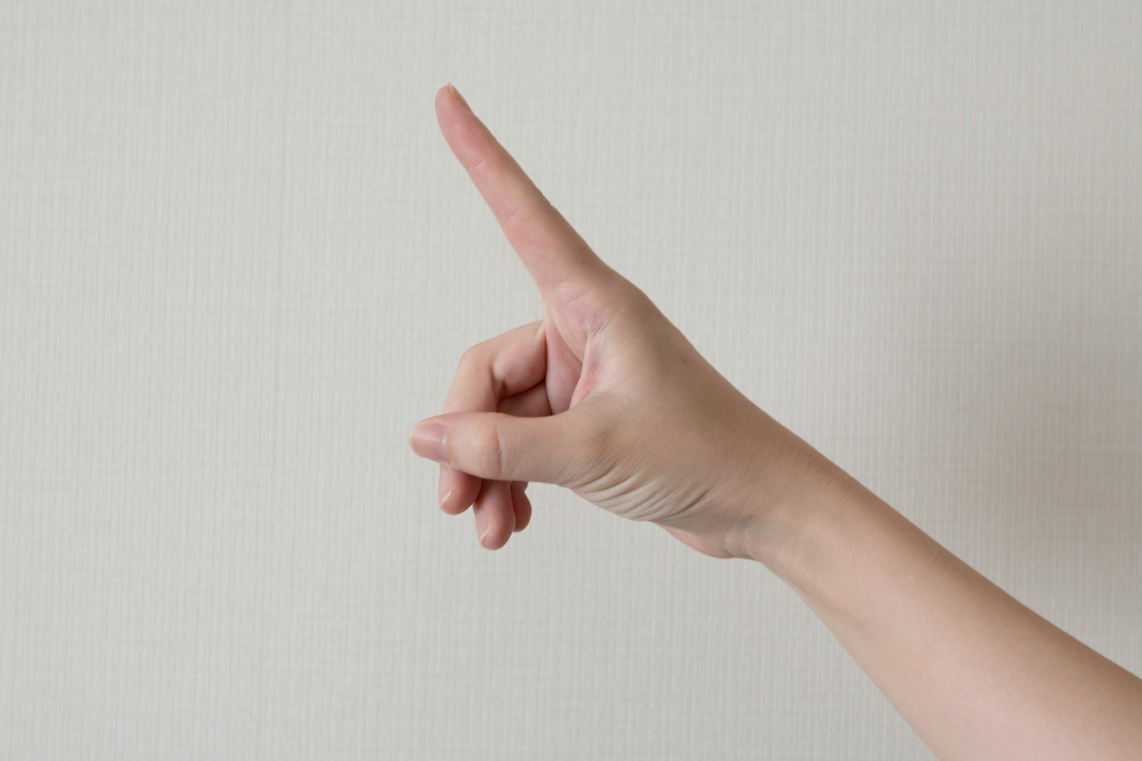 A hand with an index finger pointing upwards against a white wall