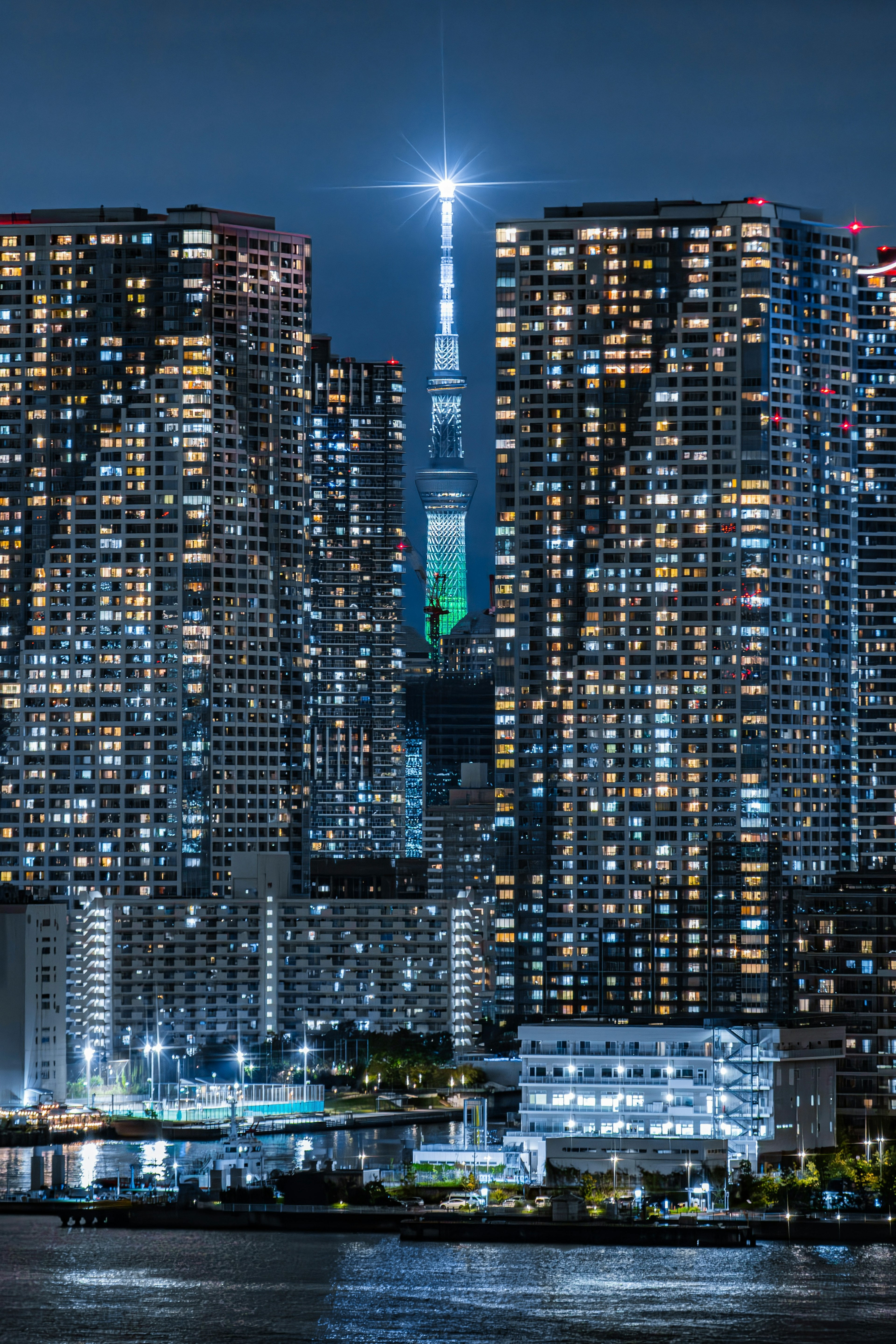 Tokyo Skytree leuchtet nachts umgeben von Wolkenkratzern und Reflexionen im Wasser