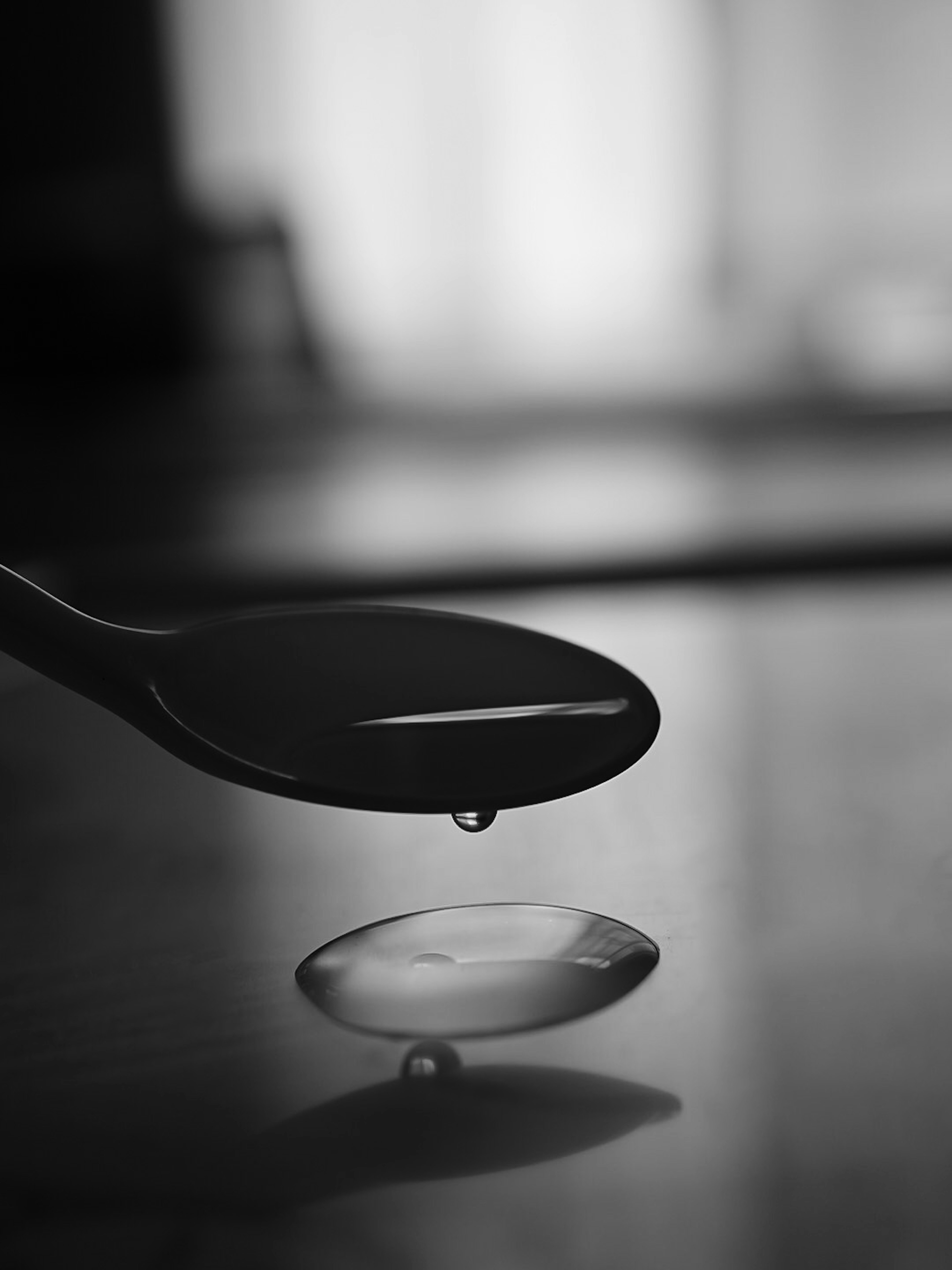 Cuchara negra con una gota de agua cayendo de su punta en blanco y negro