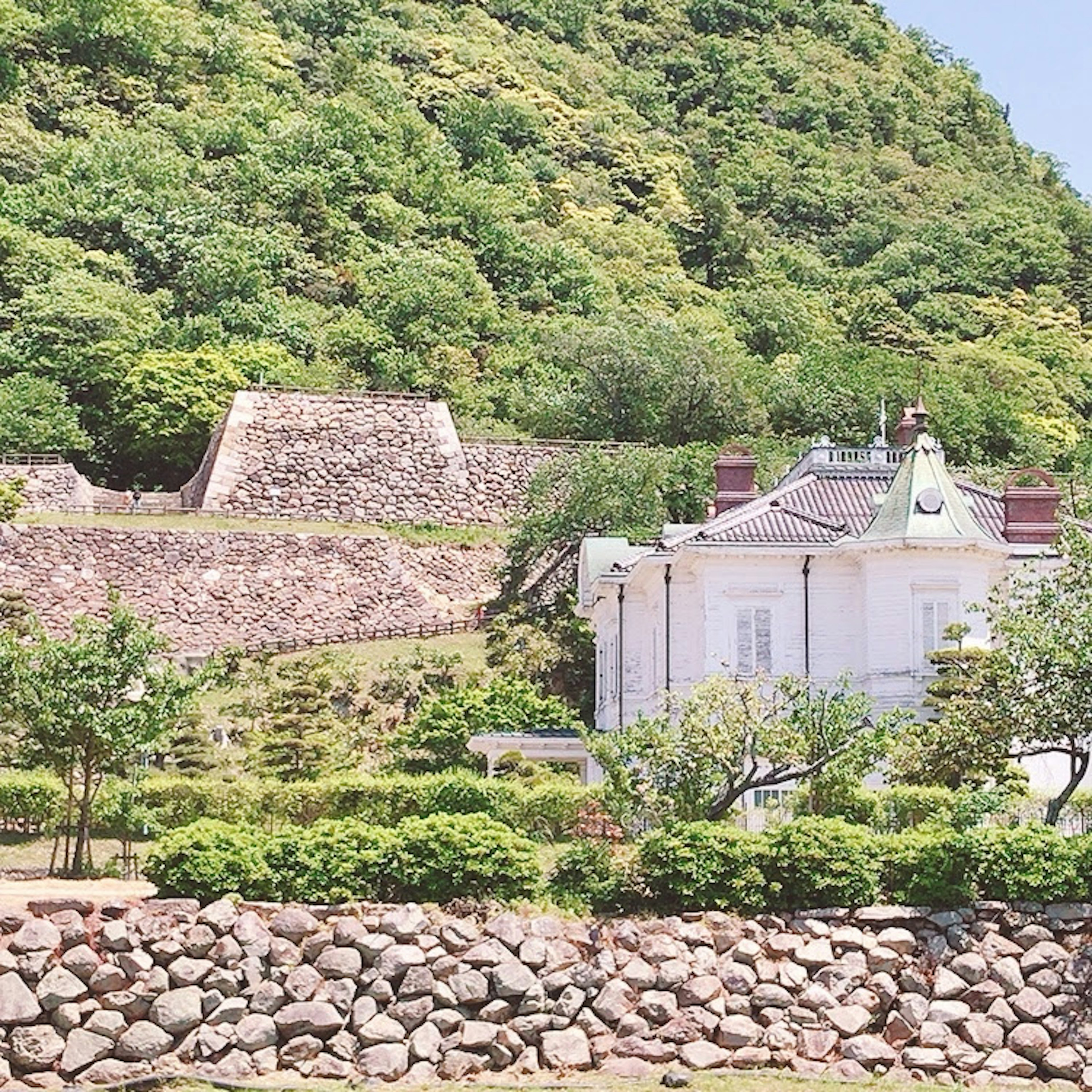 Landscape featuring a white building and stone wall against a green mountain backdrop