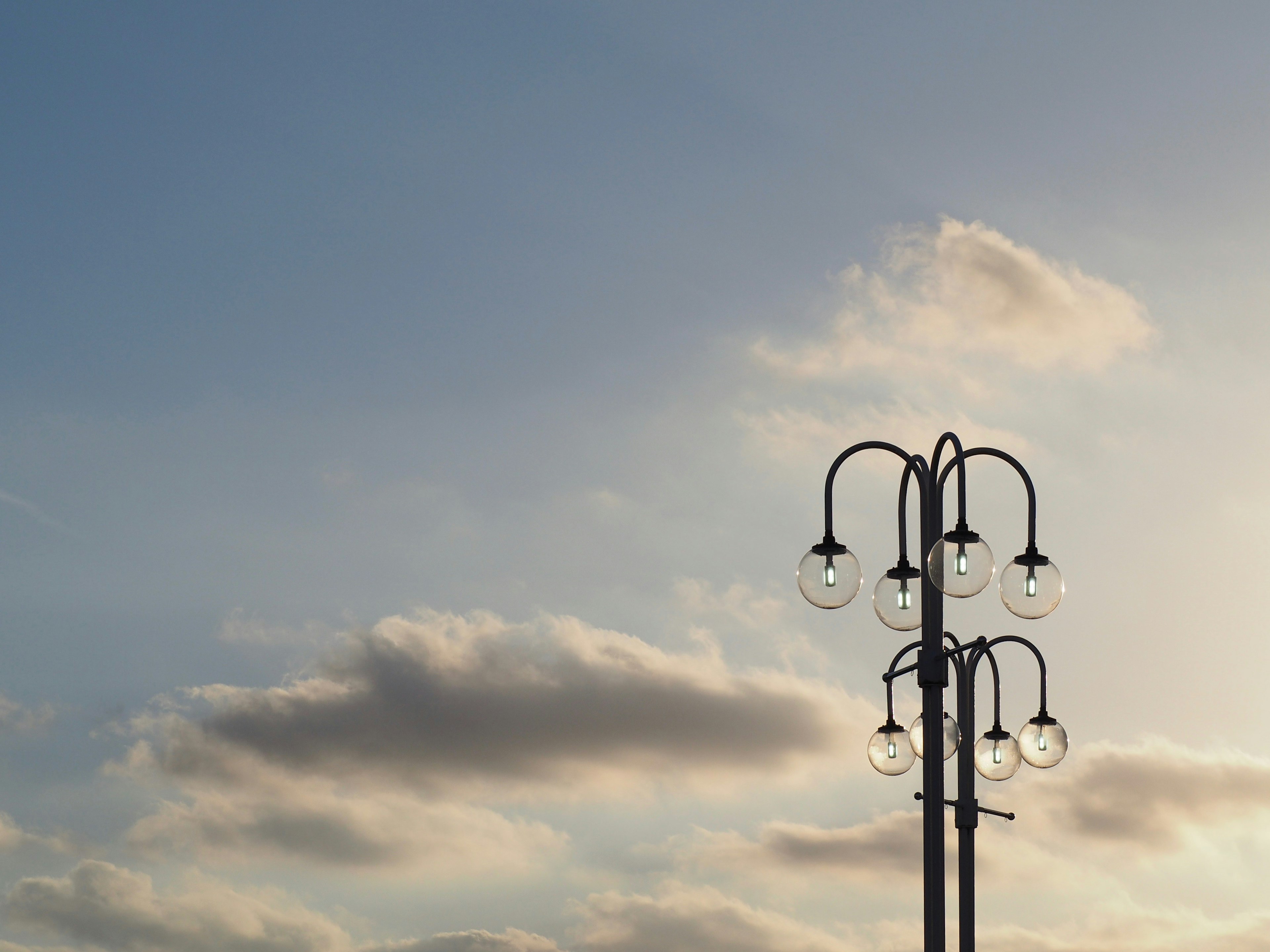 Un lampadaire avec plusieurs ampoules contre un ciel bleu et des nuages